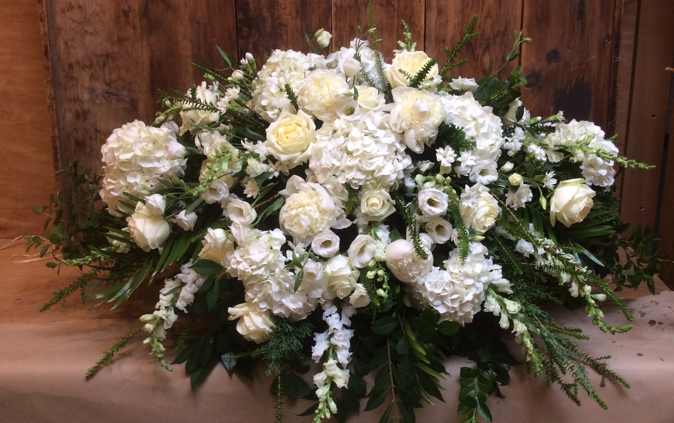White Casket Blanket - A gracious and tender tribute to a beautiful and cherished life, this elegant casket blanket radiates loveliness and serenity. Its soft and heavenly white flowers delicately speak your heartfelt emotions. White hydrangea, , white roses, white snapdragon, white alstroemeria and seasonal flowers are arranged with lush greenery.