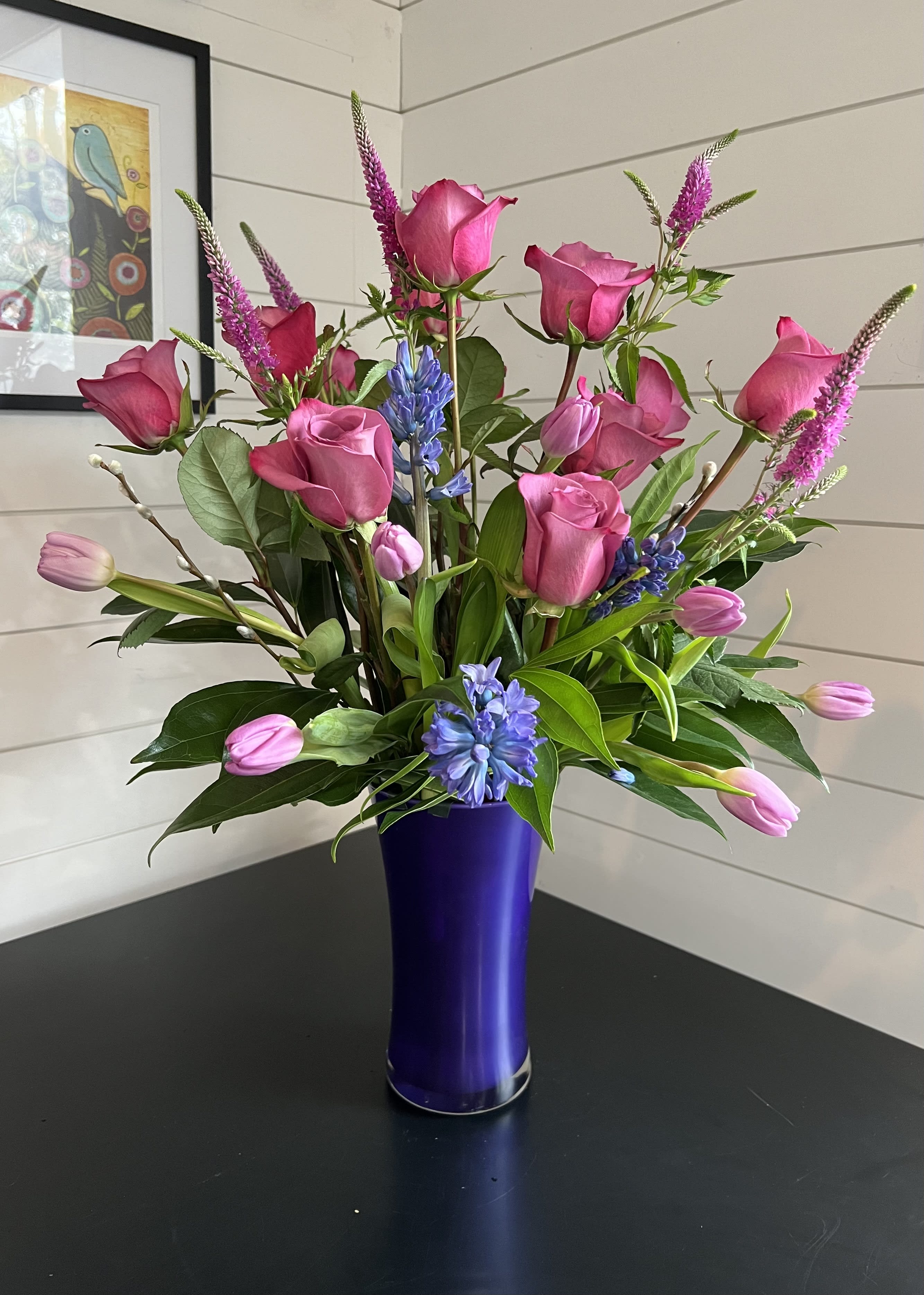 Purple Passion - One dozen lavender purple roses, tulips, veronica, hyacinth, pussy willow, assorted greenery in a matching purple vase.