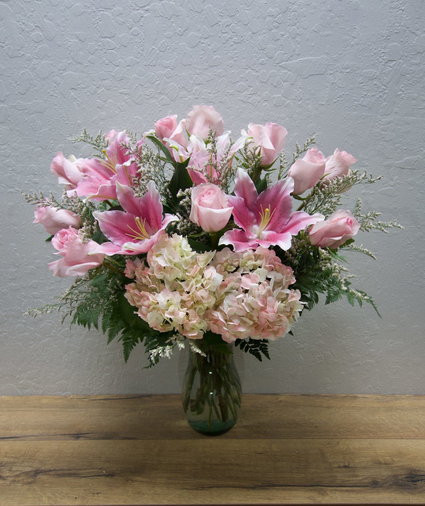 Pink Lemonade - Let these flowers remind them of the refreshing memories and love shared. This arrangement features roses, stargazer lilies, hydrangeas and mixed foliage.  Standard (as shown): 12 roses Deluxe: 15 roses Premium 18 roses