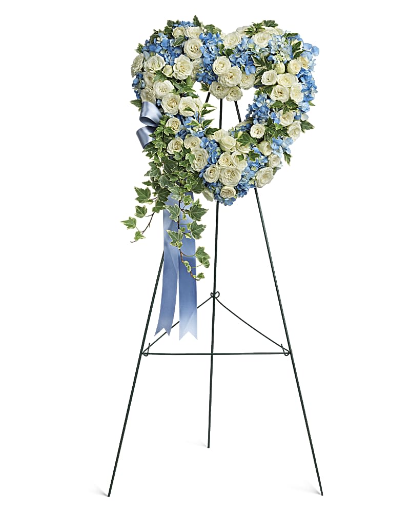 Gentle Heart - Adorned with trailing ivy, this sweet heart-shaped wreath of sky blue hydrangea and pure white roses is a loving remembrance.  This heartfelt arrangement features blue hydrangea, white spray roses, and variegated ivy.