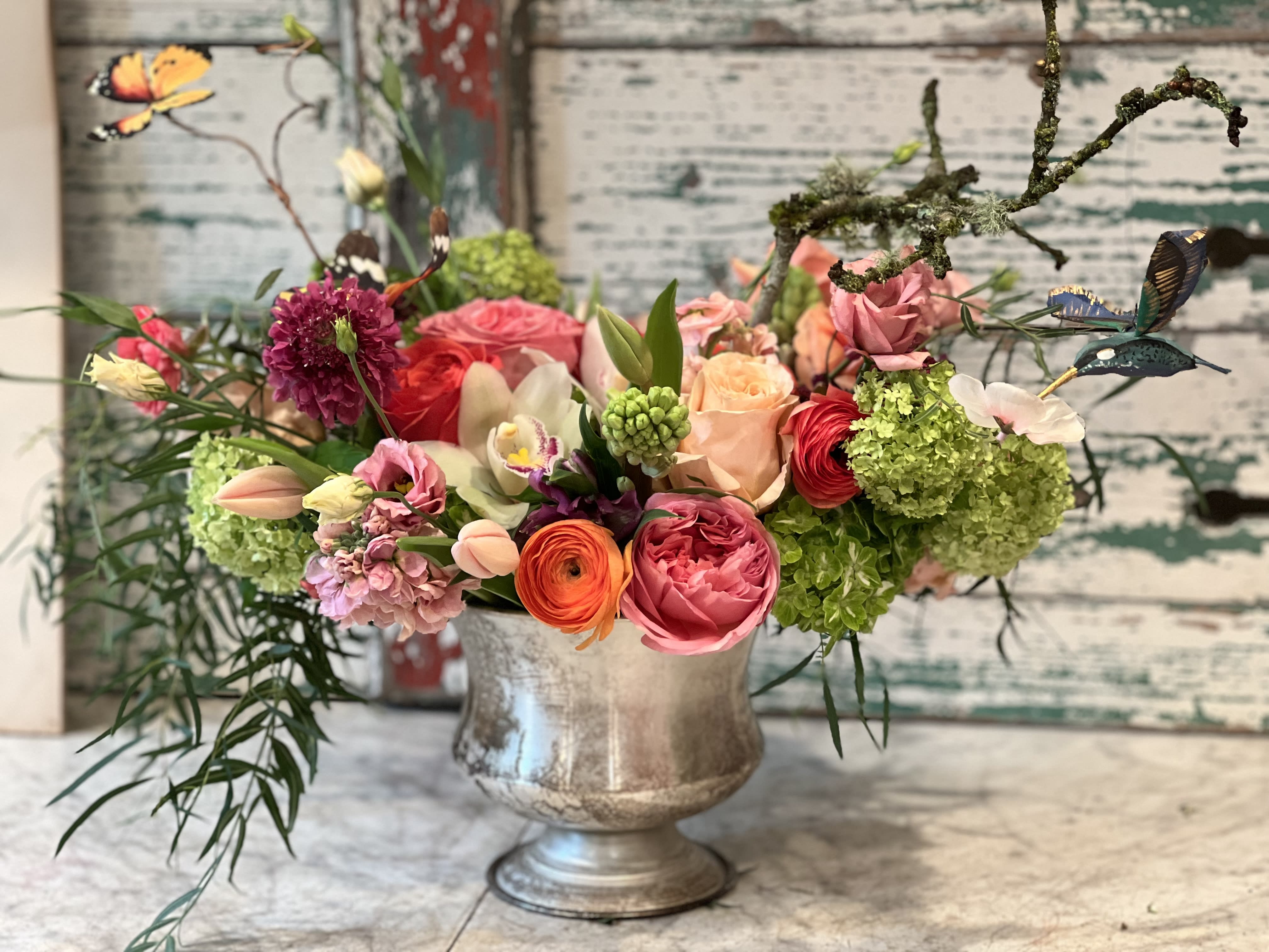 Medium silver urn filled with spring summer premium blossoms  - This is a perfect arrangement to cheer anyone for any occasion  Assorted roses orchid ranunculus and other fun blossoms