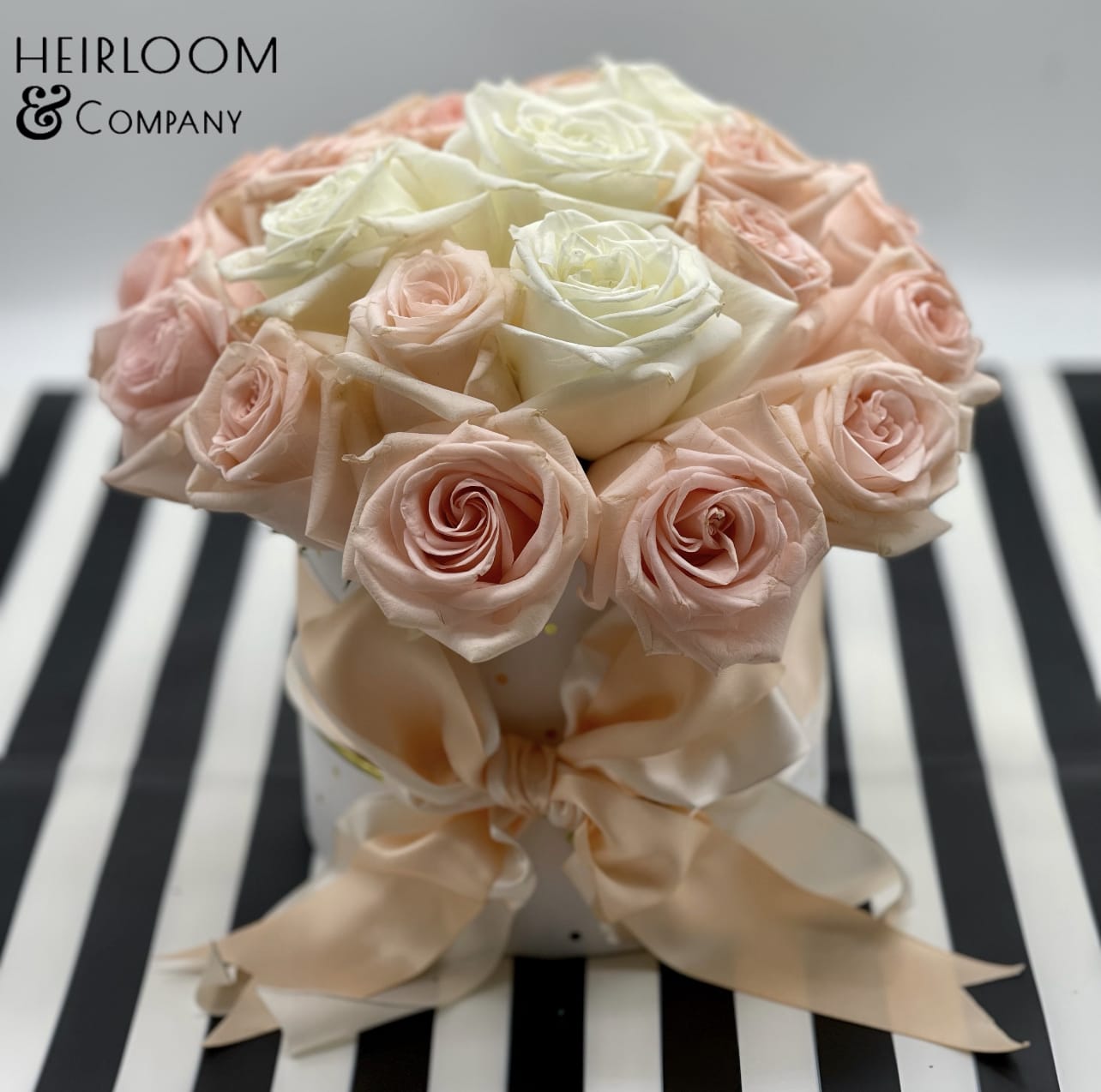 Lucy in the sky with diamonds - This adorable Arrangement is presented in a white hat box with gold shimmer polkadots, and wrapped with a double layer peach and ivory fluffy satin bow. It is filled with almost premium hand-picked blush and white garden-variety roses.