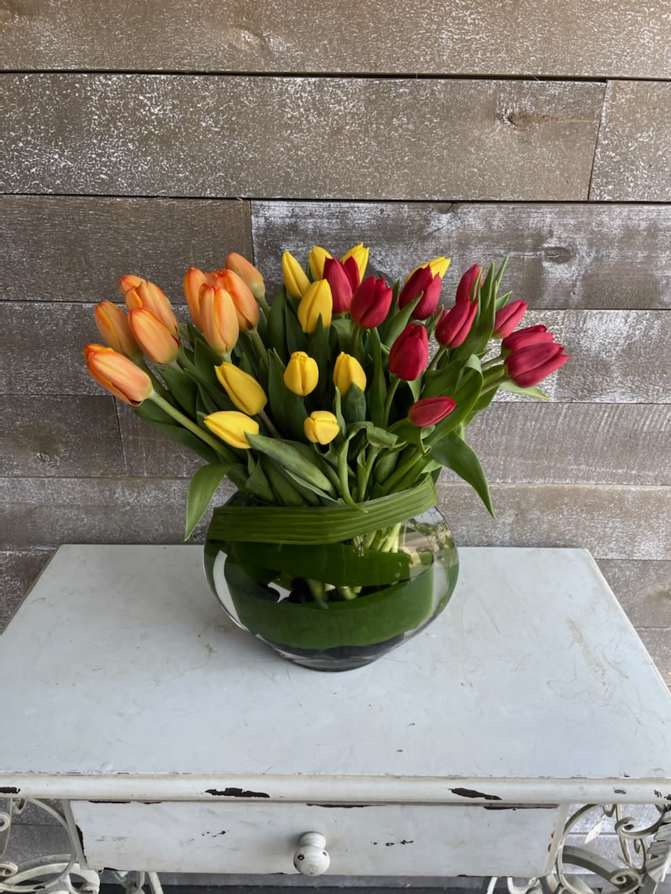 Round Tulip Trio - 3 shades of tulips organized beautifully in a bubble bowl with complimenting tropical leaves in and outside of the container. Purely Magical