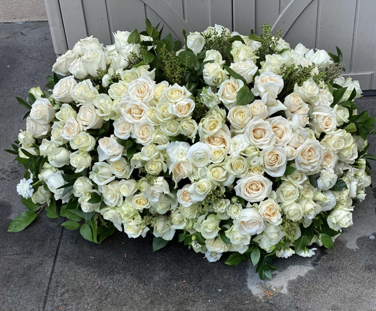 Eternal white serenity - This extra grand funeral arrangement is a stunning tribute to honor the life of a loved one. It boasts an impressive display of 100 exquisite roses and delicate white flowers, carefully arranged to convey your deepest sympathies and respect.  The soft, pristine petals of the white flowers serve as a symbol of purity, peace, and eternal love, while the bold and vibrant roses represent the strong and enduring bond you share with the deceased. The arrangement's beauty is enhanced by its size, making it an impactful centerpiece that will leave a lasting impression on all who see it.  Crafted with the utmost care and attention to detail, this magnificent funeral arrangement is a true work of art. It is designed to evoke feelings of comfort and solace, while providing a sense of closure for family and friends. Its striking presence is a testament to the enduring legacy of the one who has passed, and a reminder that their memory will live on forever.  If you want to honor the memory of a loved one with a truly exceptional display of sympathy and support, this extra grand funeral arrangement is an exquisite choice that will truly make an impact.