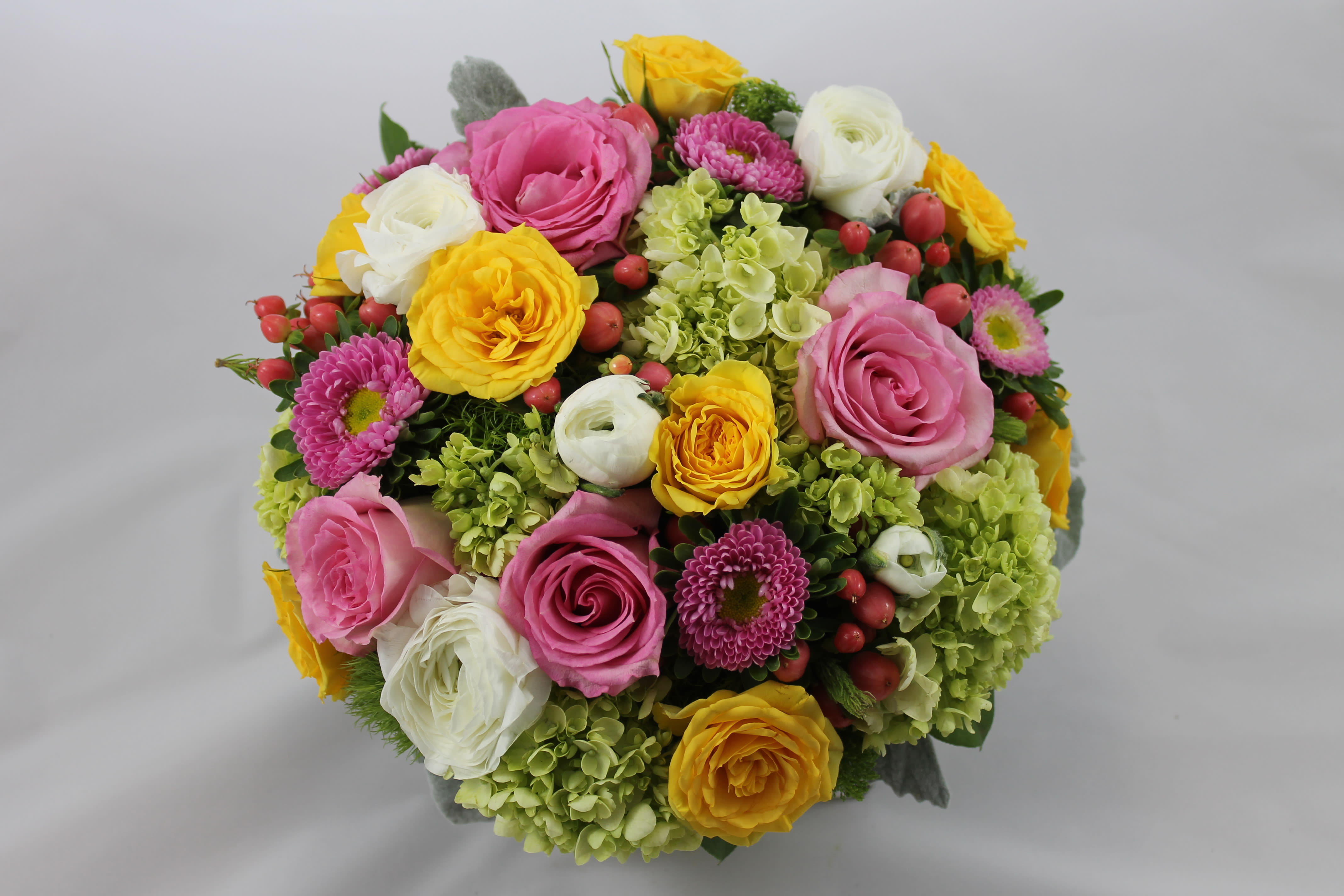 Joyous Blooms Bouquet - As the name implies this bouquet will deliver the joy to your friends and loved ones.  The bright and happy yellow and pink roses stand out against the green hydrangea and white ranunculas. Share the joy of flowers!