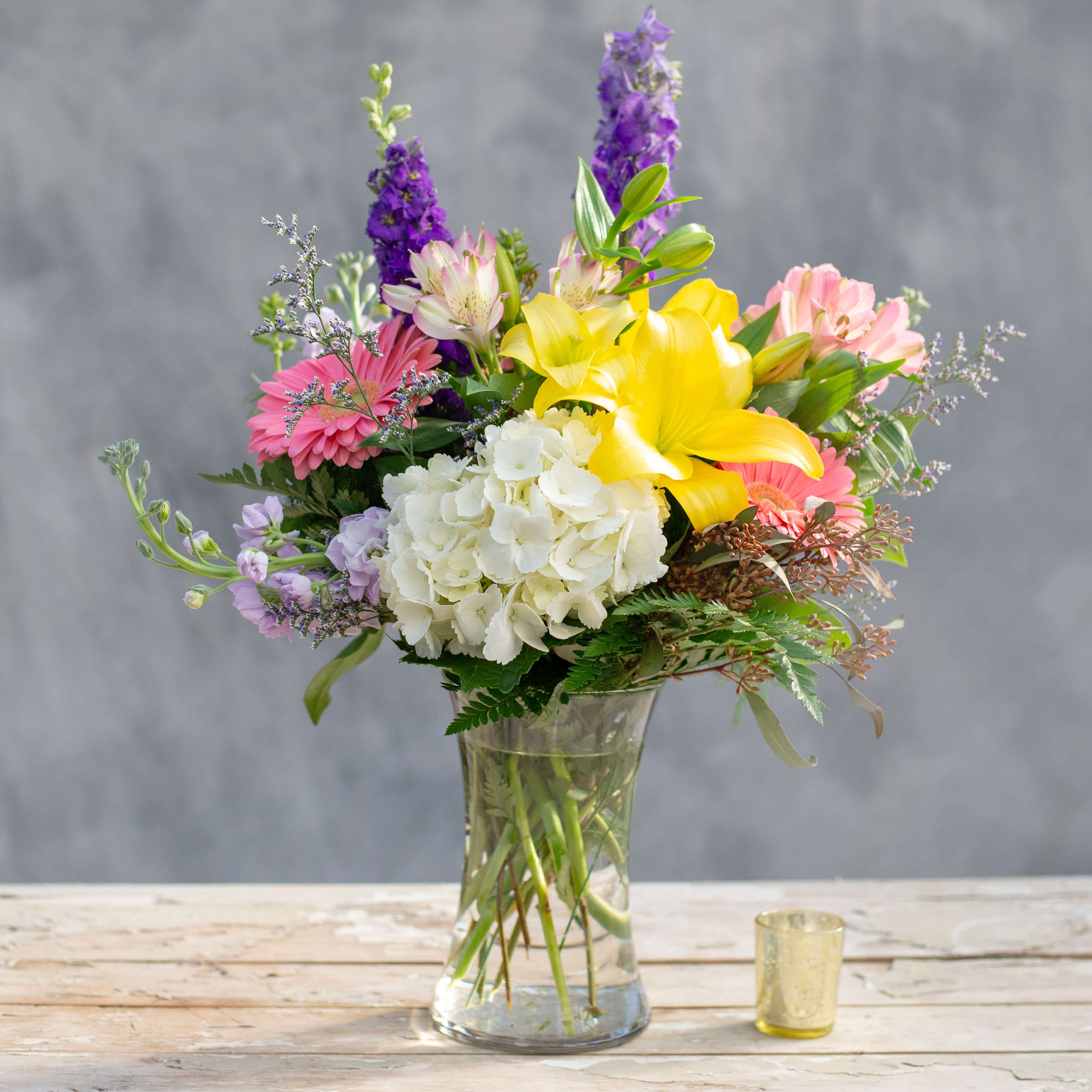 Bristow - A stunning addition to any home, apartment or office, this clear glass gathering vase, filled with the colors of Spring, purples, lavender, yellows and pink.  Flowers include, hydranga, larkspur, stock, lilies, gerbera daisies and alstroemeria.  