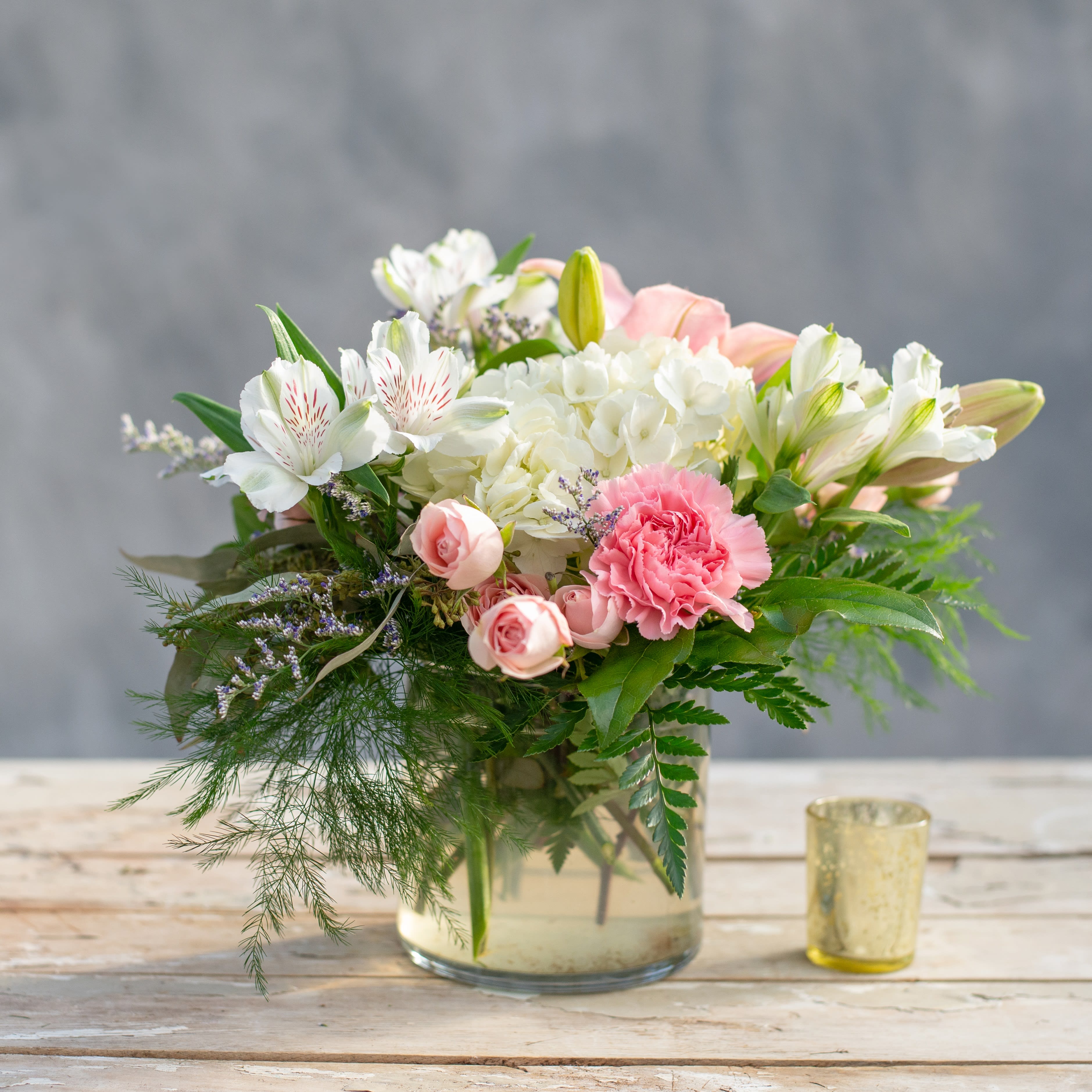 Kensington - A delicate arrangement of pinks and whites in a 5&quot; glass cylinder, including lilies, spray roses, hydrangea and more.  Perfect for a coffee, end or bedside table.  