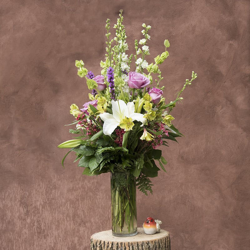 Blooming beauty - A collection of seasonal flowers in ivory lavender and white that will bring instant happiness to anyone that receives it. Roses, lilies and other fresh market picked flower selections adorned by garden greens. 