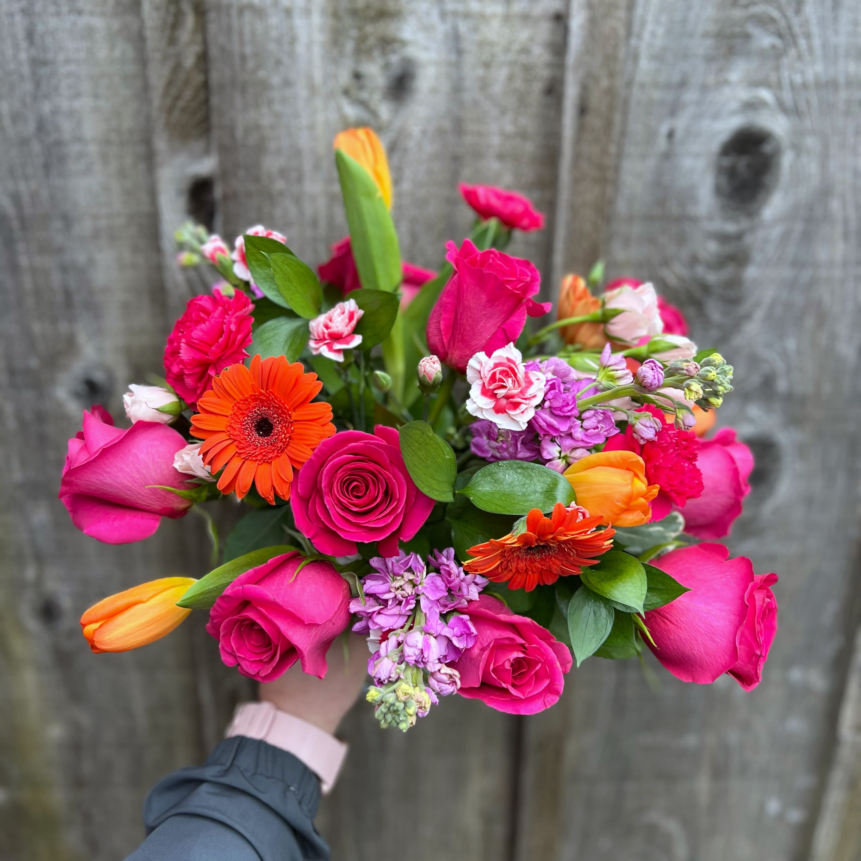 Fiesta Bouquet - Bright arrangement of hot pink and orange florals arranged carefully in a cylinder vase. Design varies upon availability and sizing. Premium product is shown. The actual product may differ slightly to the photo but will match its size and theme.