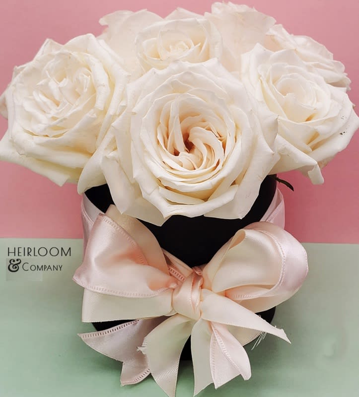 Madeline Madeline - This Hat box was inspired by one of the sweetest orders have received. Just Like Madeline herself, the roses are absolutely lovely. Consisting of Premium White Vendela and Garden Roses, this one lives in a Black Matte Hat box tied together in a Blush & White double layered Satin Bow.