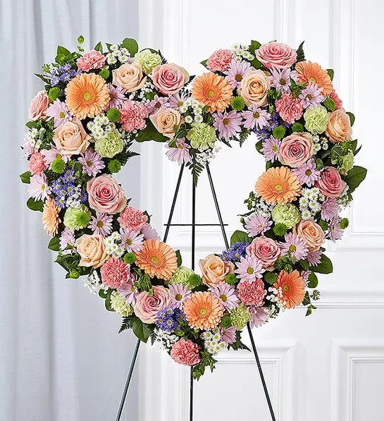 Remember Forever Floral Heart Tribute - Pastel - For the Service - The warm and gentle love they showed to those around them will keep them always remembered. This sentiment is best captured with our standing, open heart-shaped arrangement in pastel hues. Handcrafted by our caring florists with an assortment of soft, pastel blooms, it is a magnificent tribute fitting for the funeral services.  Open, heart-shaped arrangement of pink and peach roses; pink and lime green carnations; peach Gerbera daisies; purple and white monte casino; accented with baby’s breath and soft, lush greenery. Arrangement is designed on an easel. Measures approximately 26&quot;H x 28&quot;W without easel. Appropriate for the funeral home. Our florists use only the freshest flowers available, so colors and varieties may vary.