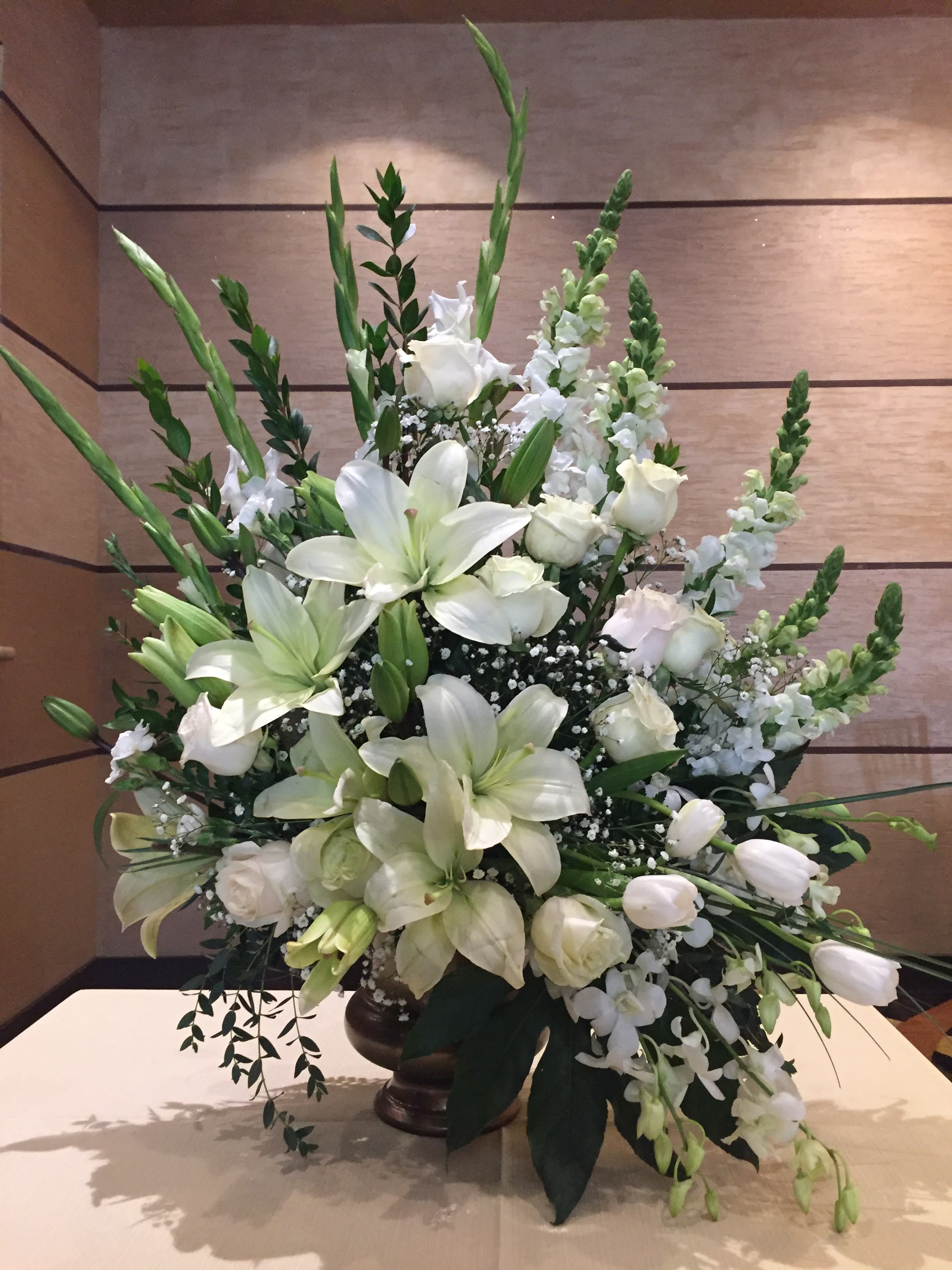 True Horizon  - As hopeful as the bright horizon ahead, this glorious white bouquet of roses, lilies, tulips, dendrobium orchids,  gladiolas and snapdragons is a peaceful tribute to a truly beloved.   •White tulips, white roses, white asiatic lilies, white snapdragons, white gladiolas and white dendrobium orchids are arranged with baby breath, seeded eucalyptus, spiral eucalyptus, green ti leaves, and lemon leaf.  •Delivered in  Modern Heritage Pot.  •Orientation: One-Sided SUBSTITUTION POLICY – Always deliver the freshest flowers! Please note the bouquet pictured reflects our original design.  If the exact flowers or container in this arrangement are not available, our local florists will create a beautiful bouquet with the freshest available flowers.