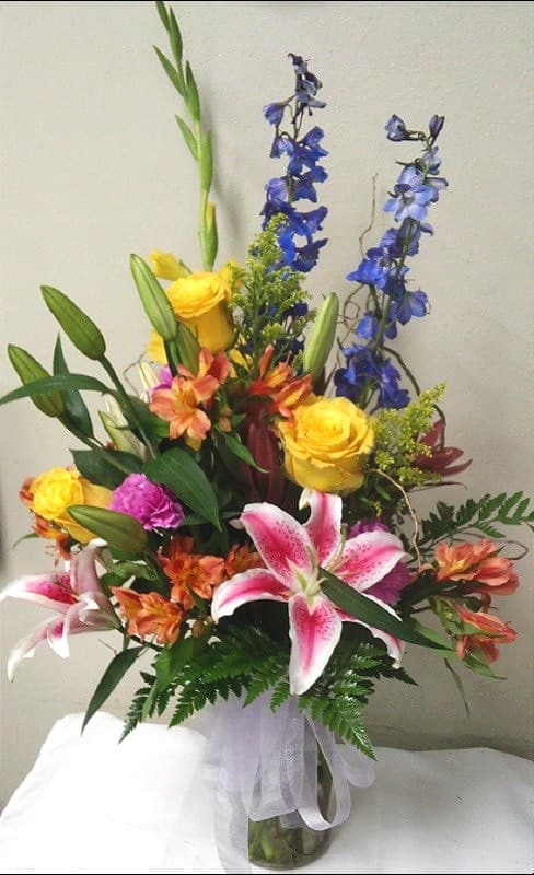 Pretty as You Please  - This Exciting Bouquet includes an Bold Mixture of Spring flowers Stargazer Lilies, Yellow Roses, Blue Delphinium, Orange tome Alstroemeria and Solidago and greens.  *Deluxe Shown  