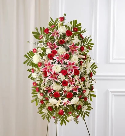 Red Rose And Lily Funeral Standing Spray - Celebrate a beautiful life with a truly heartfelt gesture. Our elegant standing sympathy spray is arranged with a gathering of radiant red, soft pink and pure white blooms. A traditional floral display for the services, it’s a touching way to honor the memory of a loved one while expressing your deepest condolences.  One-sided standing spray arrangement with red roses, pink Stargazer lilies, white Peruvian lilies (alstroemeria), carnations and football mums; accented with spiral and seeded eucalyptus, baby’s breath and assorted greenery.  Arrives on an easel. Appropriate for the funeral home or gravesite. Our florists hand-design each arrangement, so colors and varieties may vary due to local availability.