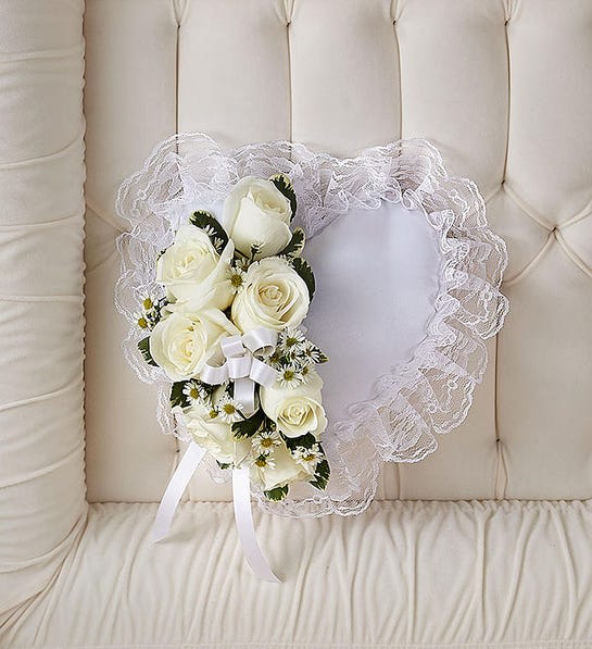White Satin Heart Casket Pillow - Our satin heart casket pillow is a way to keep one’s own heart close to someone they cared about. Fashioned by our expert florists with a spray of pristine white roses and white ribbon, this simple yet elegant arrangement is a touching ornamental gesture.  Heart-shaped satin casket pillow is adorned with a spray of white roses, baby’s breath, ribbon and soft, lush greenery Measures approximately 9”L x 9”W Appropriate for the funeral home Our florists use only the freshest flowers available, so colors and varieties may vary  Colors can be customized. Please leave specific notes in the instruction panel at checkout. 