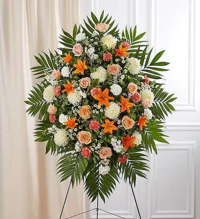 Peach, Orange &amp; White Funeral Standing Spray - For the Service - They drew people in with their welcoming smile and personality. That joyful spirit is captured in our classic standing spray arrangement. Crafted with warm orange, peach and white blooms, this elegant display creates a touching tribute to someone who brought happiness to so many.  One-sided standing spray arrangement with peach roses, orange Asiatic lilies and carnations, white football mums, stock, carnations and monte casino; accented with assorted greenery.  Arrives on an easel. Appropriate for the funeral home or gravesite. Our florists hand-design each arrangement, so colors and varieties may vary due to local availability.