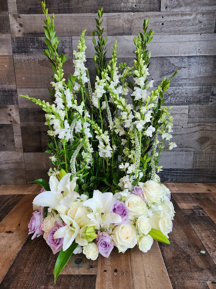 Timeless Garden Urn Wreath Timeless Garden Urn Wreath - Shown as Standard A soft color palette of white and lavender. The design is more compact in the front as to not cover the urn and taller in the back to create a garden of floral surrounding the urn. Appropriate for the service *We custom design this arrangement and use the freshest flowers available the day of delivery. The arrangement in this picture is an example of the size and style and may not feature the exact product shown.*
