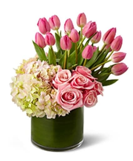 DELIGHTFUL DREAM BOUQUET  -  This Bouquet articulates the fresh beauty of the Spring season with each vibrant petal. Beautiful bunches of pink tulips, pink roses and blush hydrangea are artfully arranged in a clear glass cylinder vase lined with lush tropical leaves to create a most impressive display of Spring's most glorious blooms.