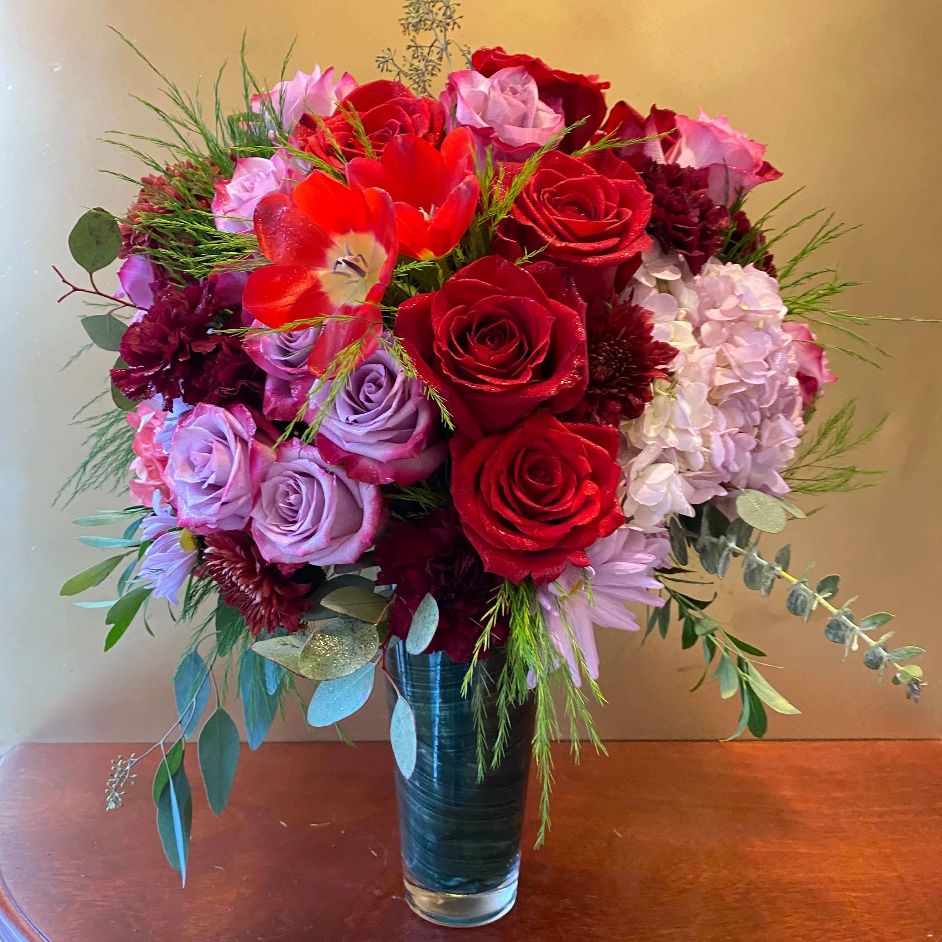 Cascading Elegance Bouquet - Make an unforgettable statement with this jewel-toned masterpiece of roses and hydrangea, presented in an elegant glass vase. Dark pink hydrangea and red roses, red spray roses, purple carnations, purple button spray chrysanthemums, and purple cushion spray chrysanthemums are arranged with hanging green amaranthus, israeli ruscus, ti leaves. SUBSTITUTION POLICY  Please note the bouquet pictured reflects our original design.  If the exact flowers or container in this arrangement are not available, will create a beautiful bouquet with the freshest available flowers.