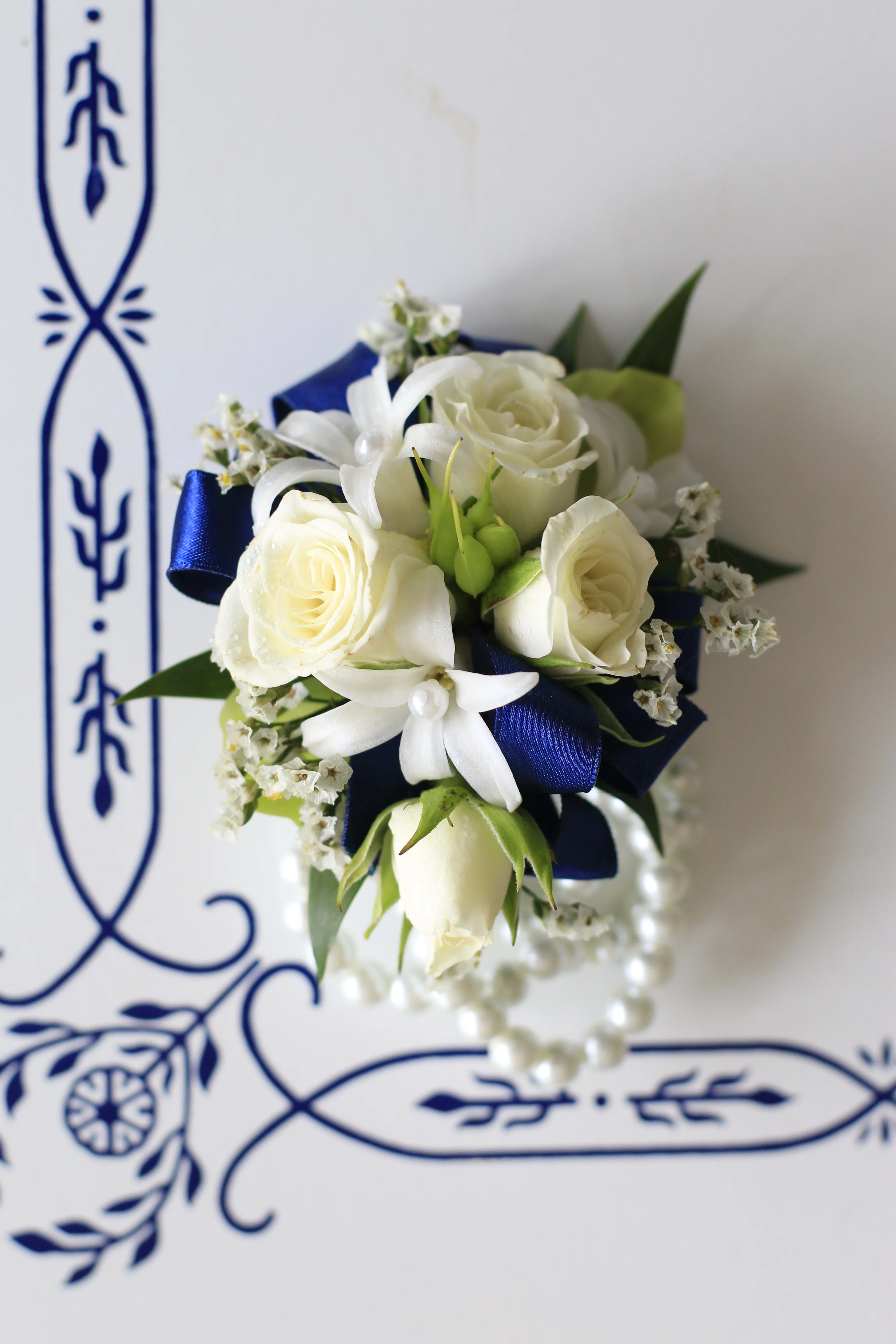 Fancy wrist corsage - White roses with accent flower on pearl band.  Accent flower may vary but will always coordinate.  PLEASE SPECIFY RIBBON COLOR IN SPECIAL INSTRUCTIONS.  COLORS AVAILABLE ARE ROYAL BLUE, WHITE, SILVER, GOLD, BLACK, LIGHT PINK.  CALL TO INQUIRE ABOUT OTHER COLORS.