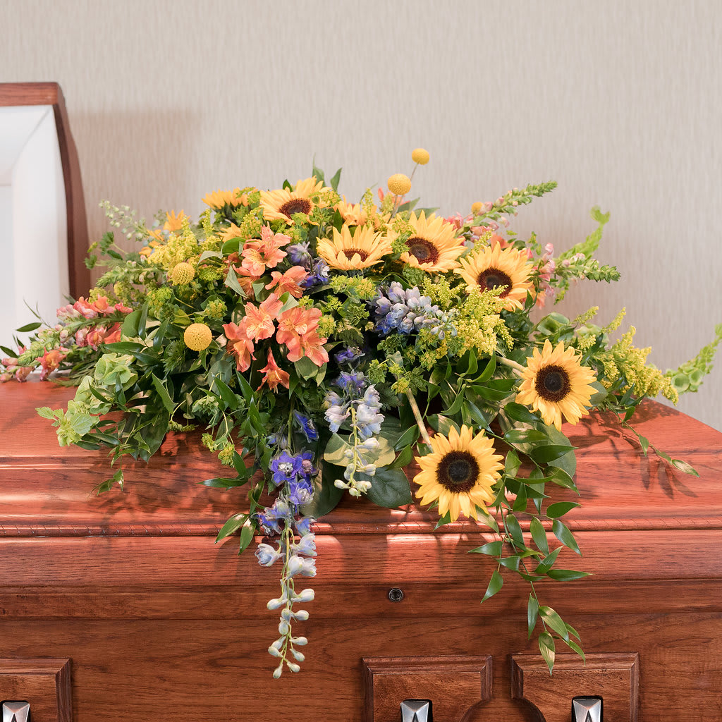 Essence - For the one who loved summer, this casket spray of sunflowers and summer blooms is the perfect way to honor them.