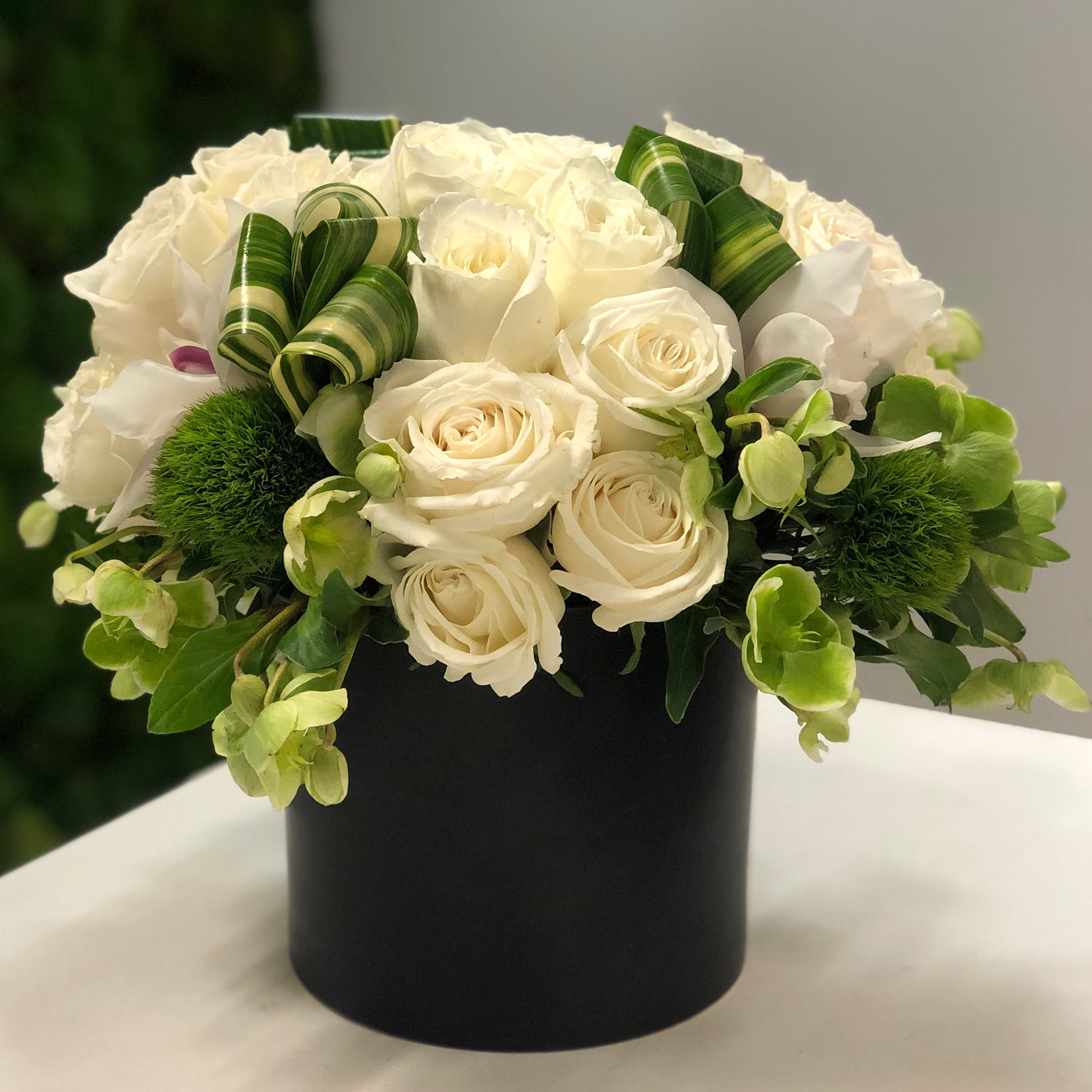 Black Matte Garden - Mixed bouquet of white roses, white orchids, hellebores, green moss and variegated aspidistra leaves arranged in a black matte ceramic 6&quot; vase. Overall arrangement height is about 12&quot;