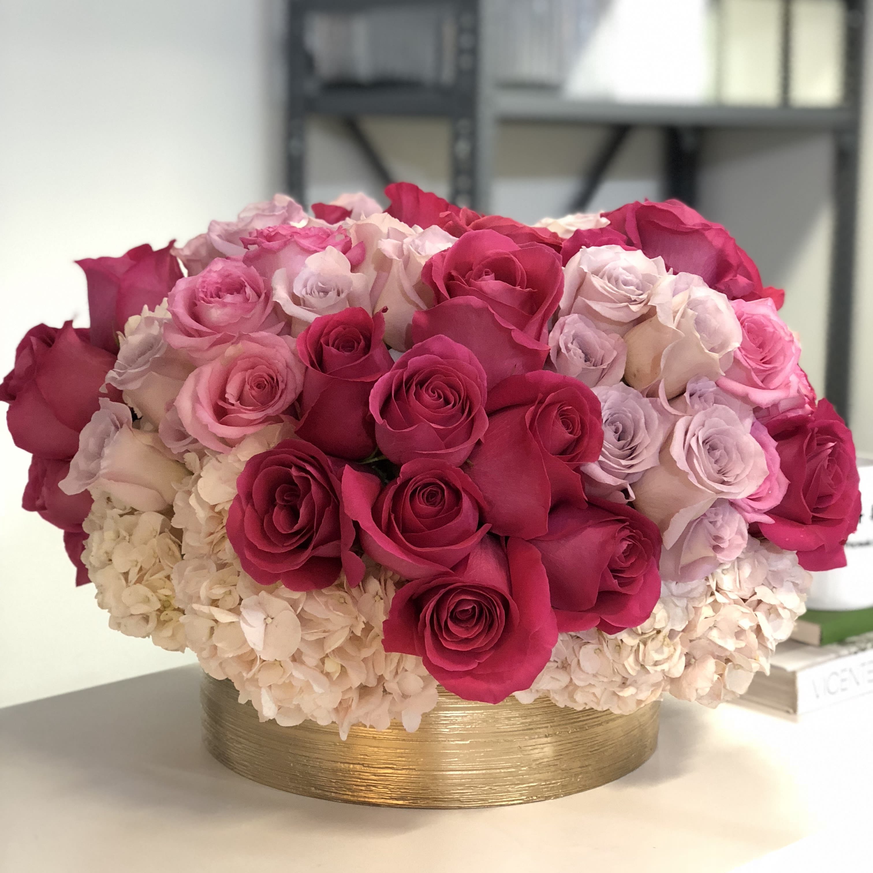 Pink Lady Pink Lady - Mixed roses in shades of hot pink, lavender, white, and bubblegum, accented with hydrangeas in a 5″H x 10″D round gold vase. Arrangement stands approximately 15″ tall.