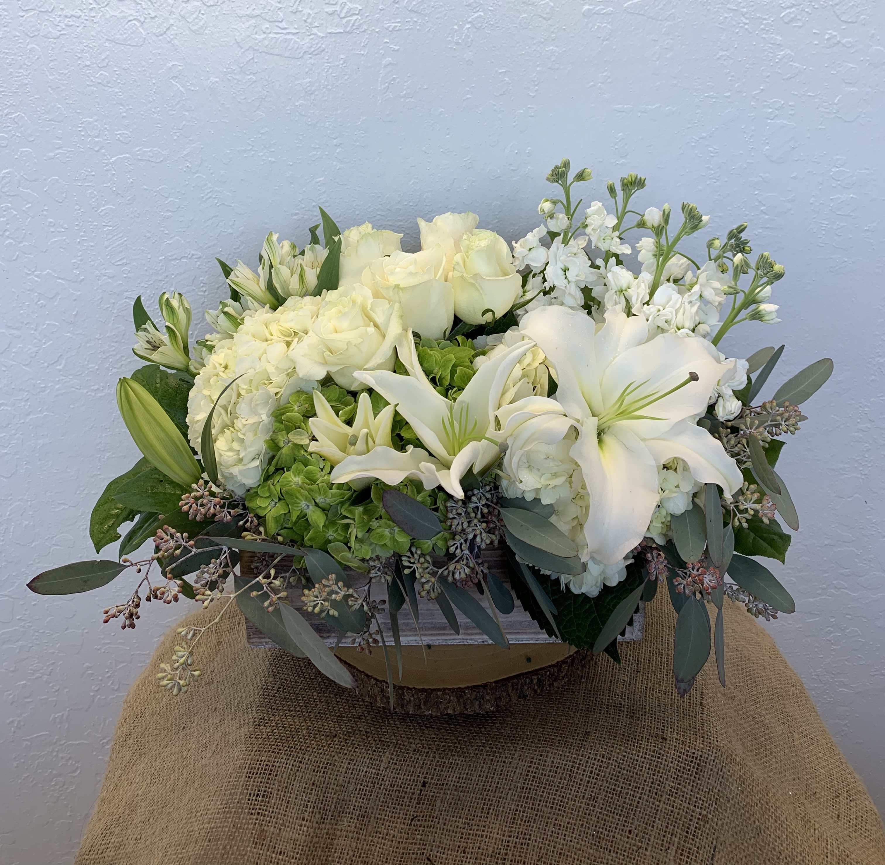 Secret Garden - White - A secret garden lies within our imaginations, a sight to behold. This unique white colored arrangement features roses, hydrangeas, lilies, alstroemerias, stock, and mixed foliage.  Deluxe (as shown) The arrangement is approximately 14&quot; H and 15&quot; W (Woodbox 12&quot; W)