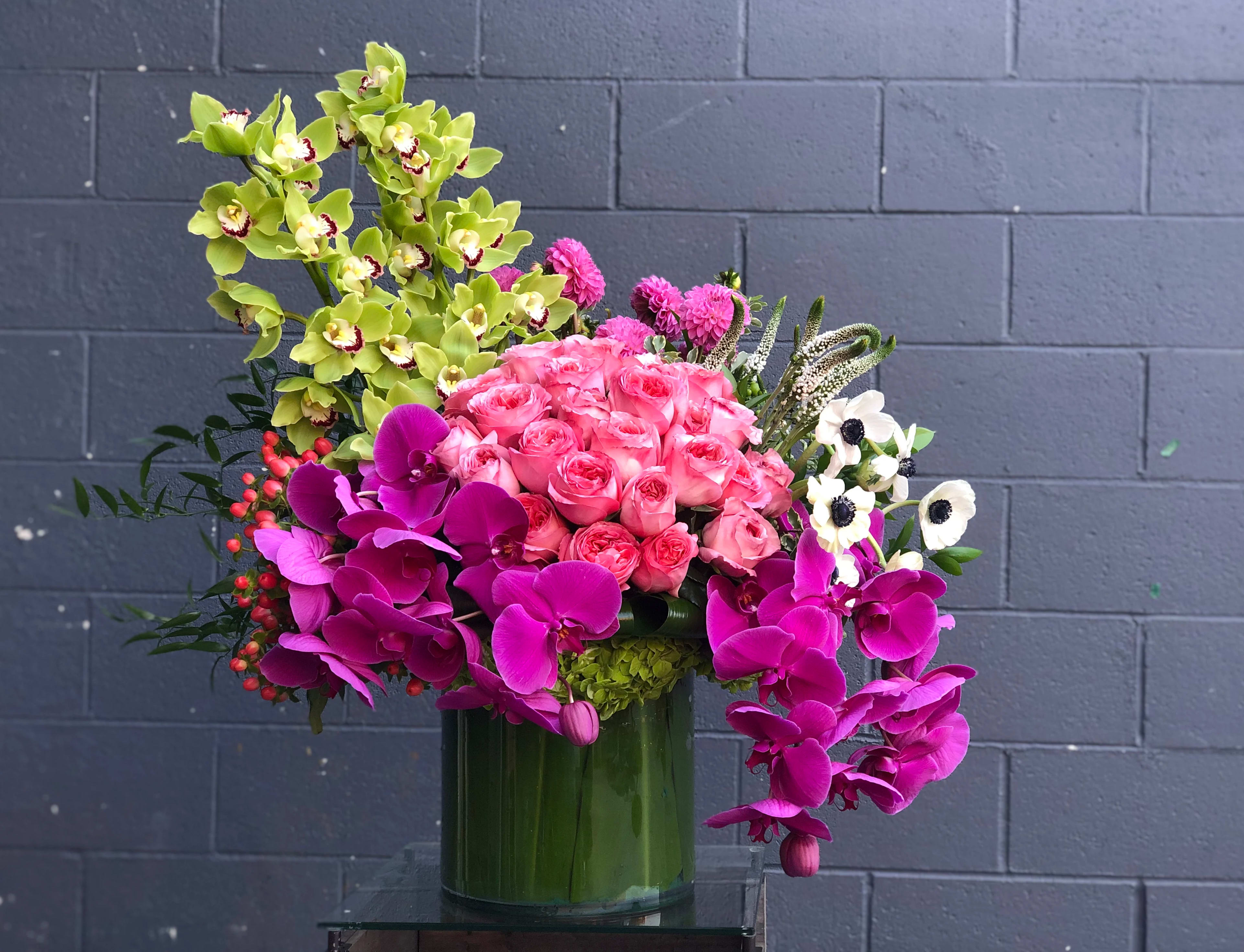 Funky Fuchsia - A bright and colorful arrangement of stunning orchids, roses, and various other luxurious blooms in a large, leaf-lined 10&quot;x10&quot; cylinder vase.