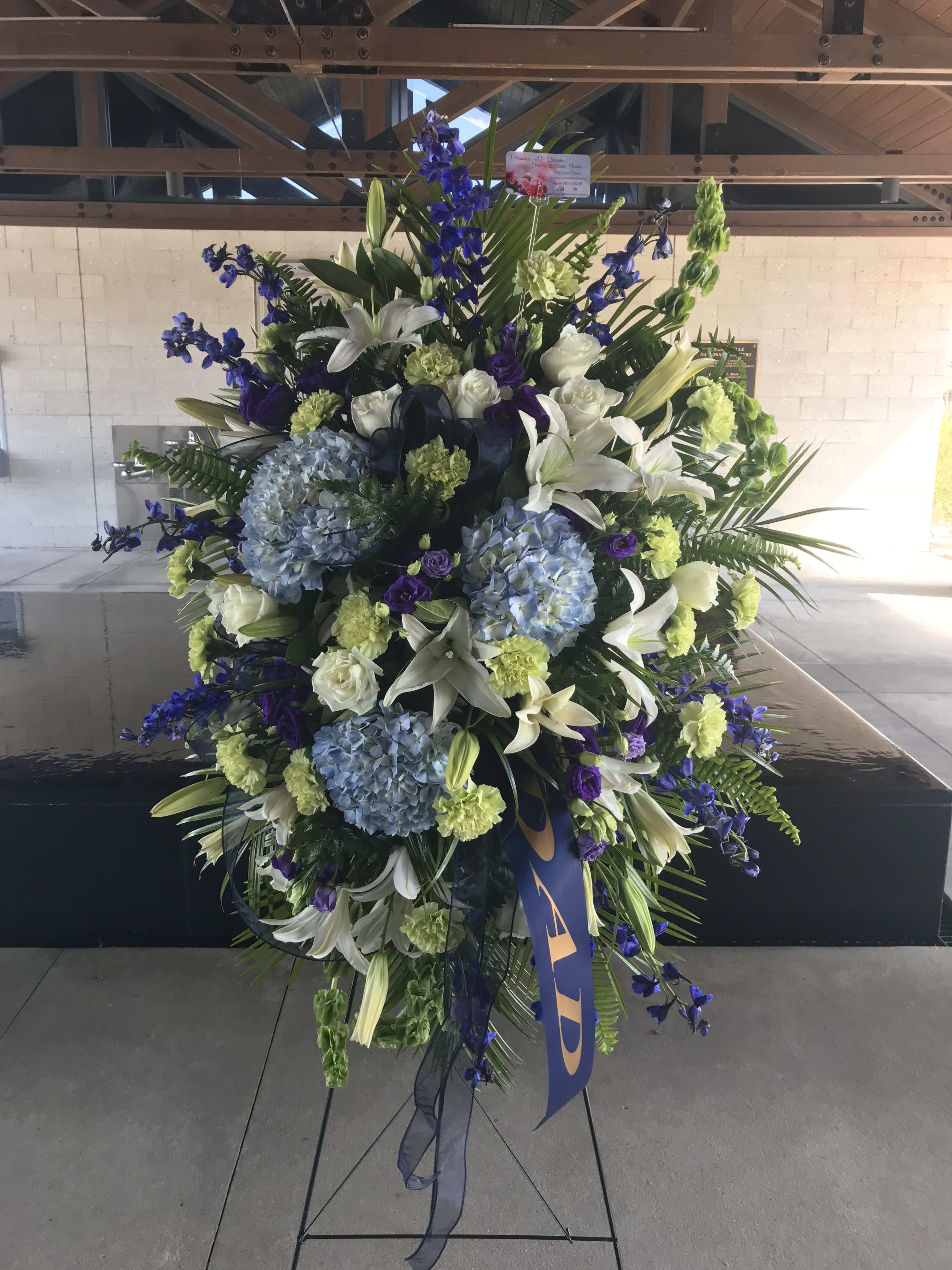 Simply Majestic Standing Spray Simply Majestic Standing Spray - When they deserve all the respect you can give, this piece reflects it. Beautiful blue hydrangeas are nestled amongst green carnations, white lilies, white roses, and lush greens. Stunning! Add a banner for that extra special touch (not included).