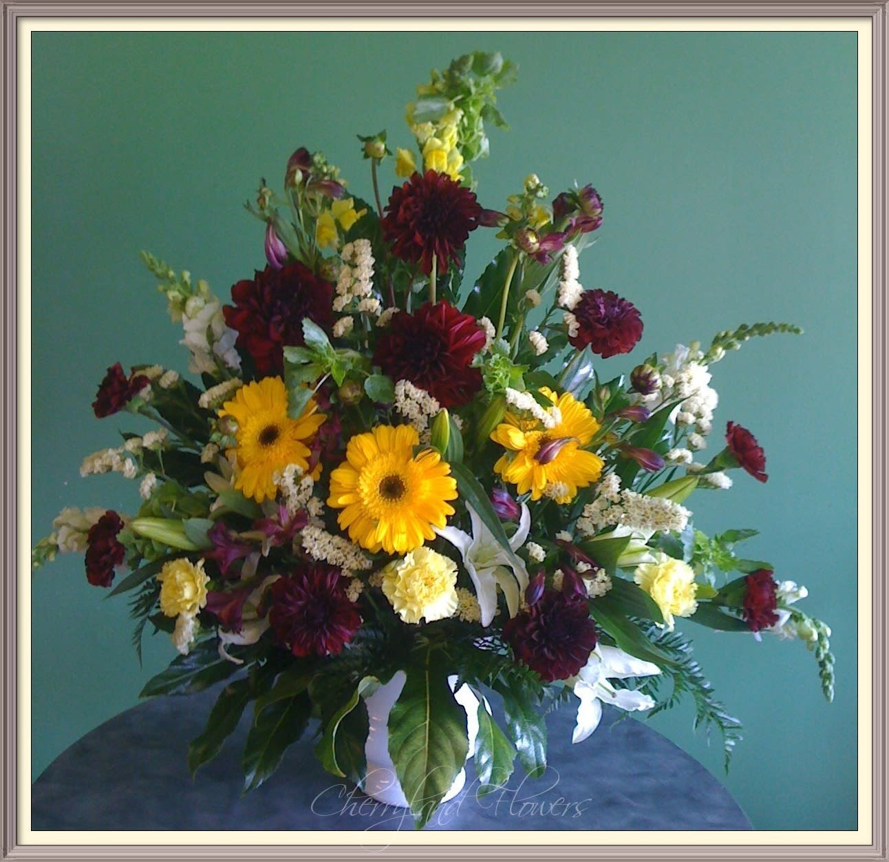 Serendipity Basket - Surprise a loved one with this vibrant maroon and yellow combination of fresh gerberas, dahlias, statice, carnations, lilies, snapdragons, and foliage artfully arranged in an elegant white container.  