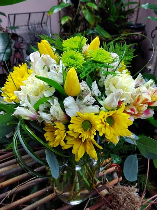 Springtime Delight - This bright and cheerful arrangement is designed using green poms, tulips, roses, daisy poms, carnations, alstroemeria, bear grass, eucalyptus, salal, and plumosa. Dimension: 12&quot;x8&quot; 