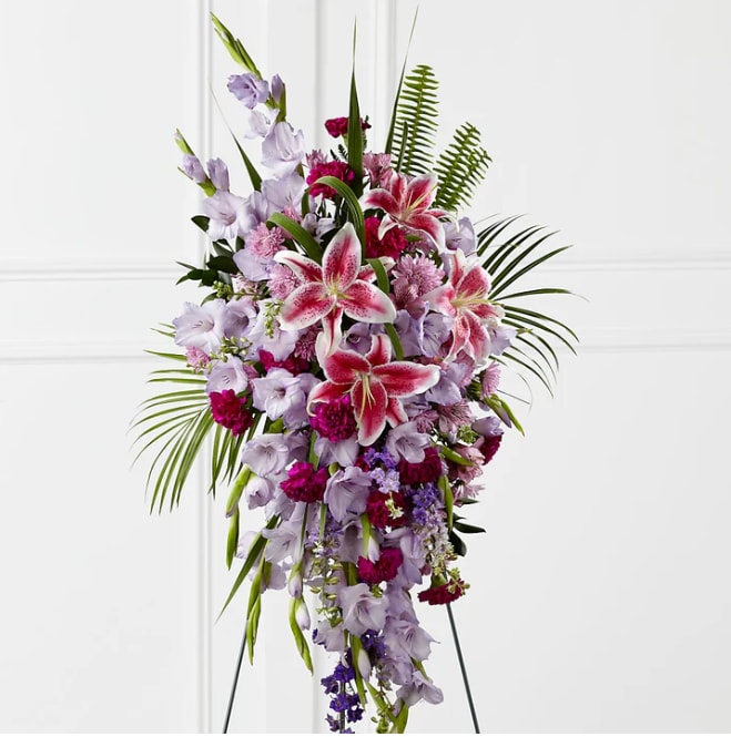 Tender Touch Standing Spray - The Tender Touch Standing Spray creates an elegant display of beauty and color to enhance their final tribute. Lavender gladiolus, Stargazer lilies, fuchsia carnations, purple larkspur, lavender Peruvian lilies, lavender chrysanthemums, sword fern fronds, emerald palm fronds and other assorted greens are gorgeously arranged to create a sophisticated standing spray. Displayed on a wire easel, this arrangement will add to the sophistication of their service with each fragrant bloom. DETAILS 52&quot;h x 28&quot;w