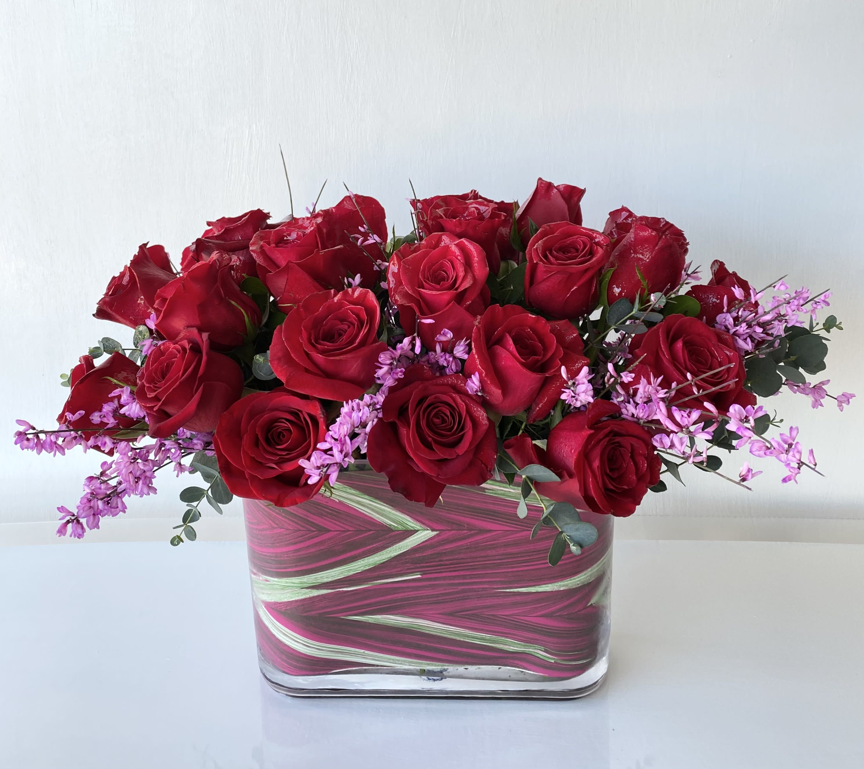 Love &amp; Happiness - An arrangement of 24 short-stemmed high-quality red roses in a 7.5&quot; by 10&quot; rectangular glass vase. Covered with a decorative faux greenery-pink liner standing at 15&quot; tall x 18&quot; wide.