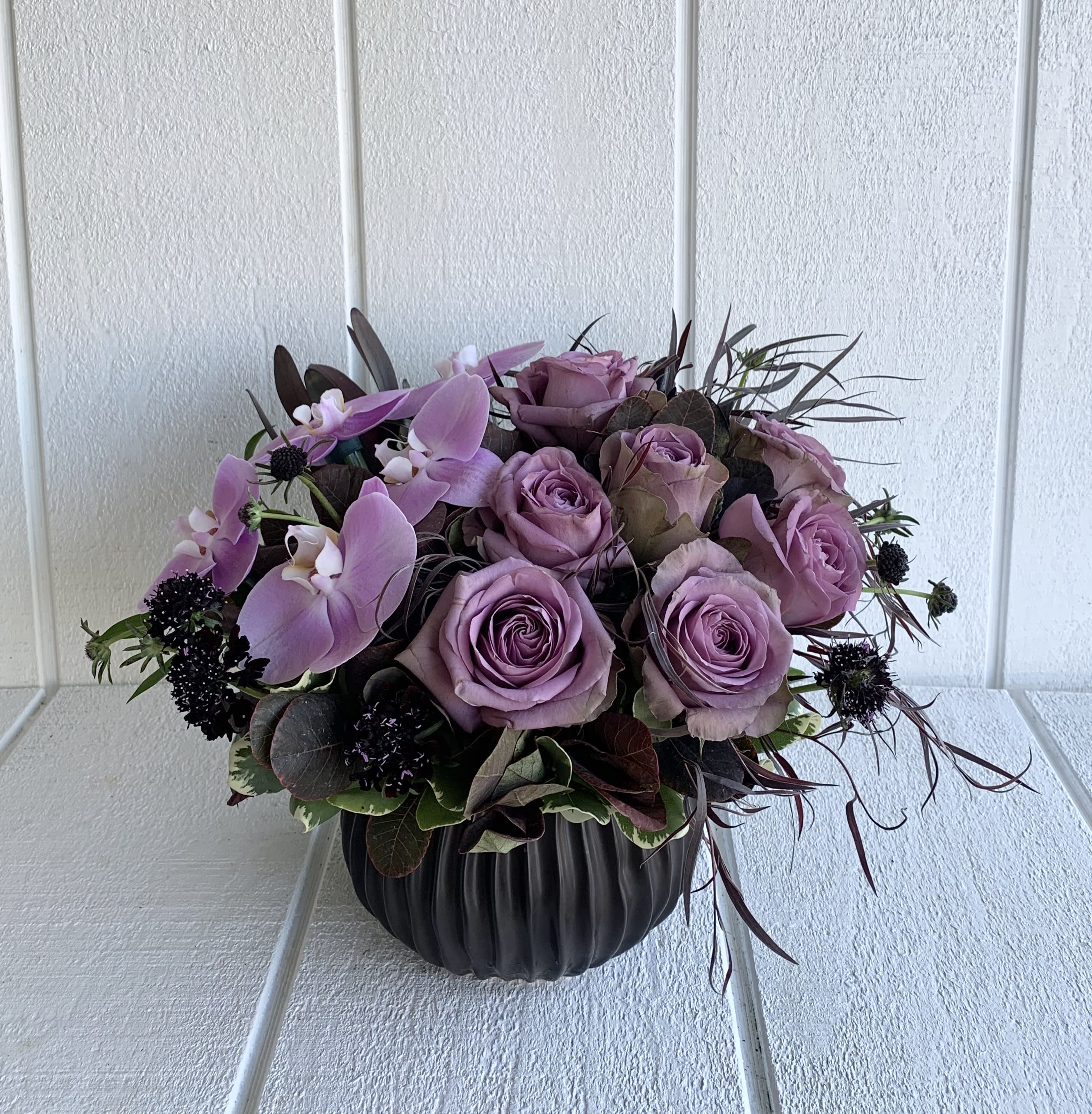 Midnight Purple - A simple gorgeous arrangement for all.  A 6&quot;H round ceramic matt black vase standing at approximately 12&quot;tall. 14&quot;wide with purple roses, pink Phalaenopsis orchid, variety blooms, and foliage.