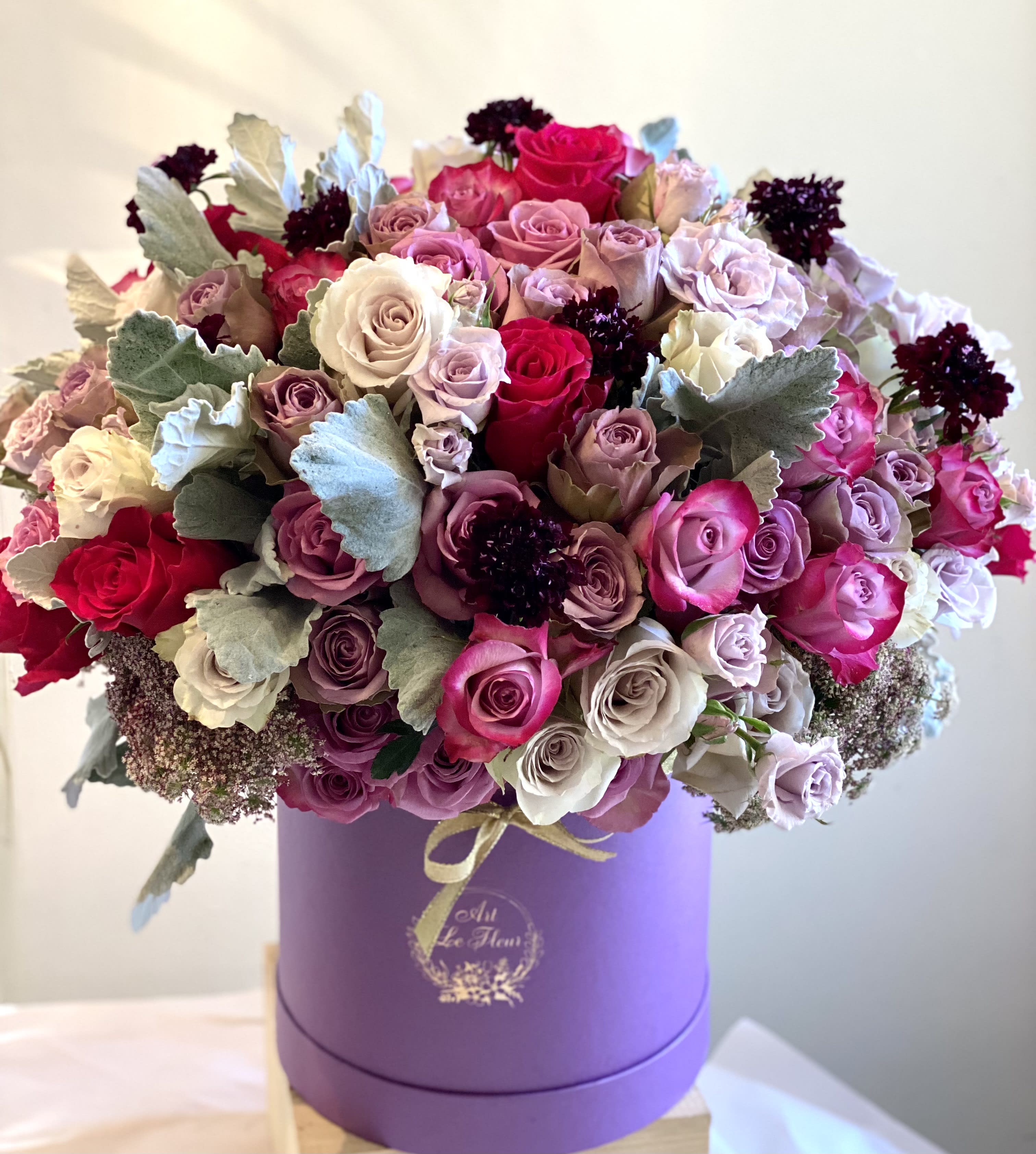 Stellar  - This floral hatbox is a fine assembling of some of our favorite varieties of roses in shades varying from sterling to deep purple, accented with the velvety dusty miller and our unique textured scabious blooms. Produced in a grand style, a perfect presentation of gratitude, commitment, celebration,  love or validation. 