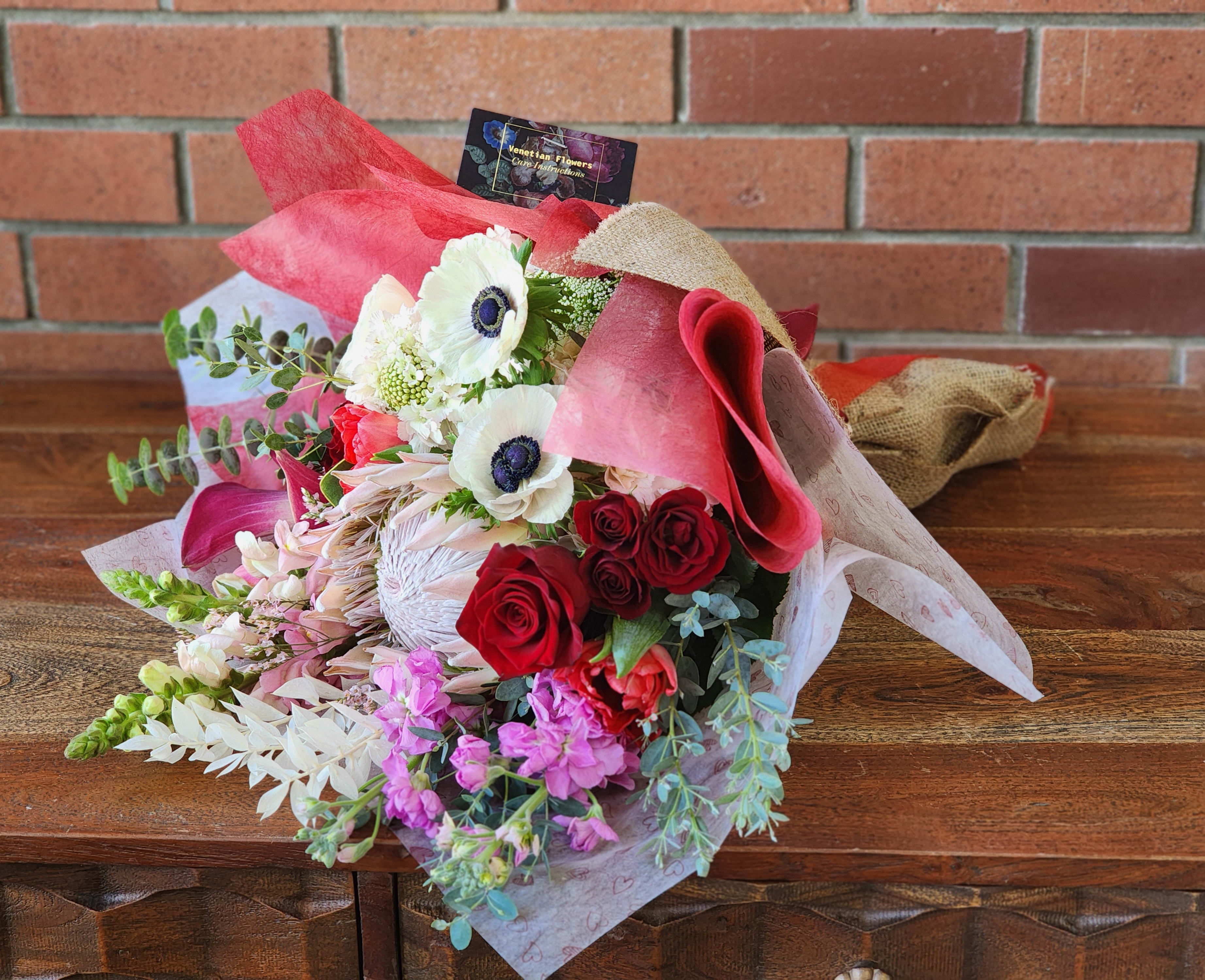 Romantic Wrapped Bouquet  - Premium lovely blooms protea, red roses, pink hydrangeas, anemones, scabiosa, stock, snap dragons, Eucalyptus tulips and more wrapped with lively Valnetine's Day paper and burlap 