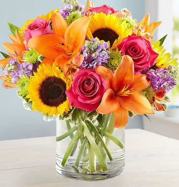 Floral Embrace Floral Embrace - Glass cylinder overflowing with sunflowers, stock, roses, alstroemeris and mums