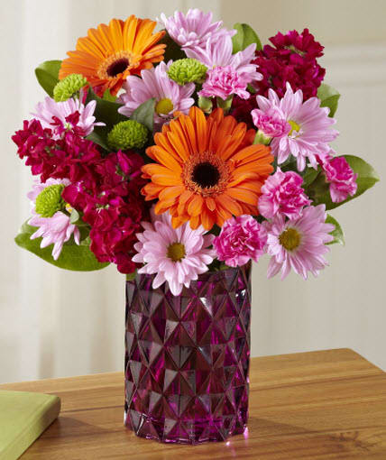 The FTD Brightly Bejeweled Bouquet The FTD Brightly Bejeweled Bouquet - This mixed flower arrangement is sure to attract plenty of admiring attention with Gerbera daisies, stock, carnations and roses and more beautifully hand-arranged in a glass vase that sparkles like amethyst colored gemstones.