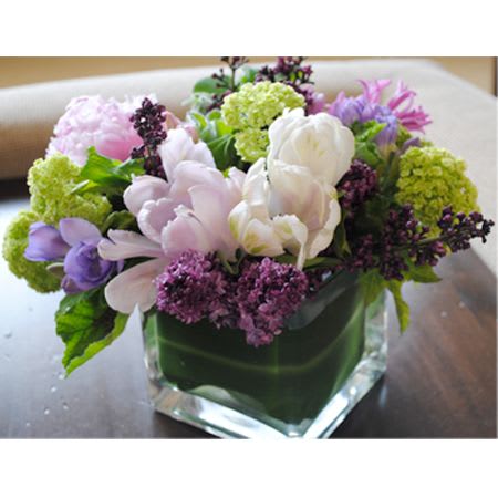 Spring is in the Air - This stunning arrangement is made in a leaf lined glass cube. It has a beautiful assortment of all the high end spring flowers including Lilacs, Parrot Tulips, Viburnum &amp; other seasonal flowers. 