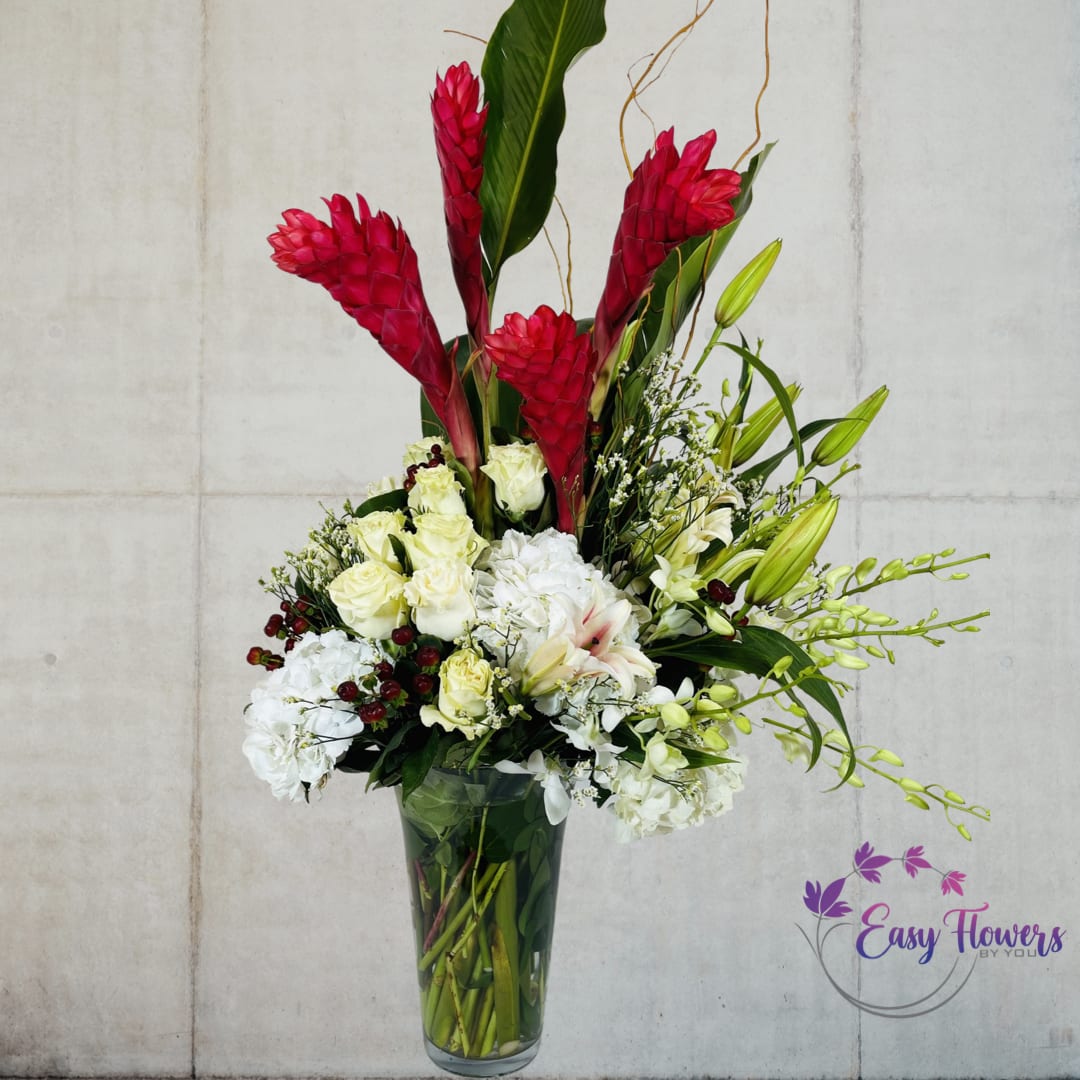 Natural Artistry - Experience a burst of vibrant colors with our exotic flower arrangement featuring Ecuadorian red roses, white hydrangea, red ginger, and white oriental lilies. This stunning floral display is presented in a tall, clear glass vase and accentuated with sprigs of curly willow vine, orchids, and tropical leaves. Perfect for adding a touch of elegance to any occasion or decor.