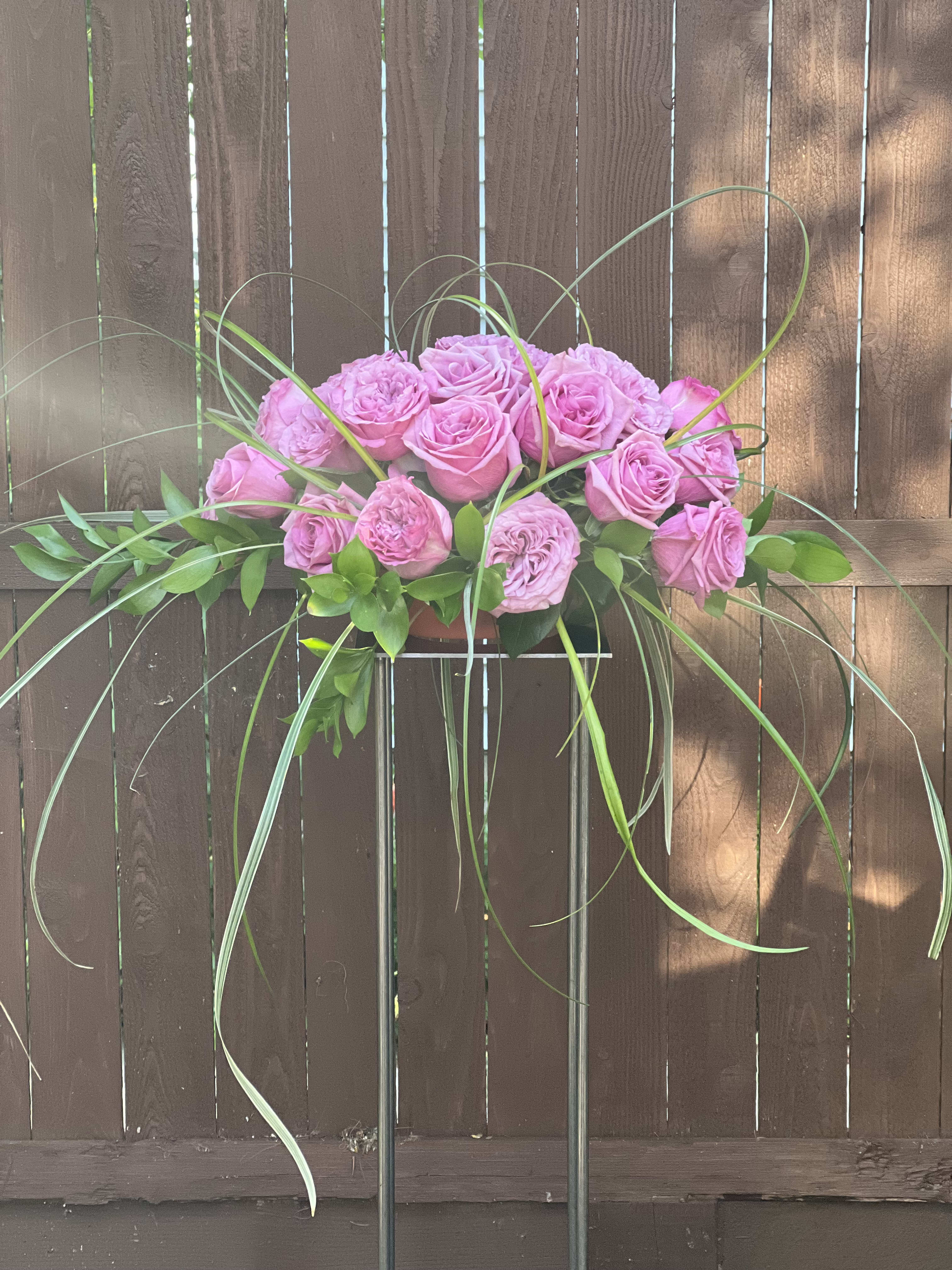 Exquisite  (Special order ONLY)  - Exquisite starts with a metal Harlow Stand. (instead of purchasing the stand, it can also be rented)  CALL FOR PRICING.  A plastic tray holds the foam that anchored a mix of 25 roses, greenery and accents into the container. Perfect for a entryway, wedding, alter or outdoor event. Can be created with different color roses. This is just and example with lavender roses and garden roses mixed with greenery.