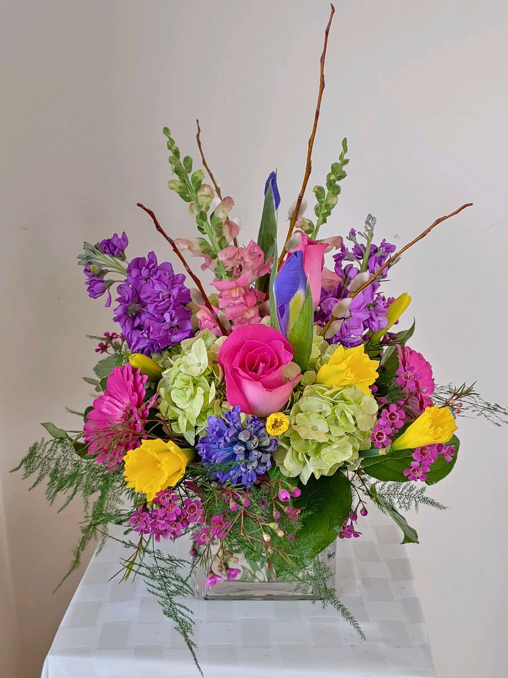 Green Hydrangea,Deep Lavender Stock,Yellow Daffodills,Hot Pink Rosesand Spring Pussywillows. - A clear cube arrangement with an assortement of spring flowers.