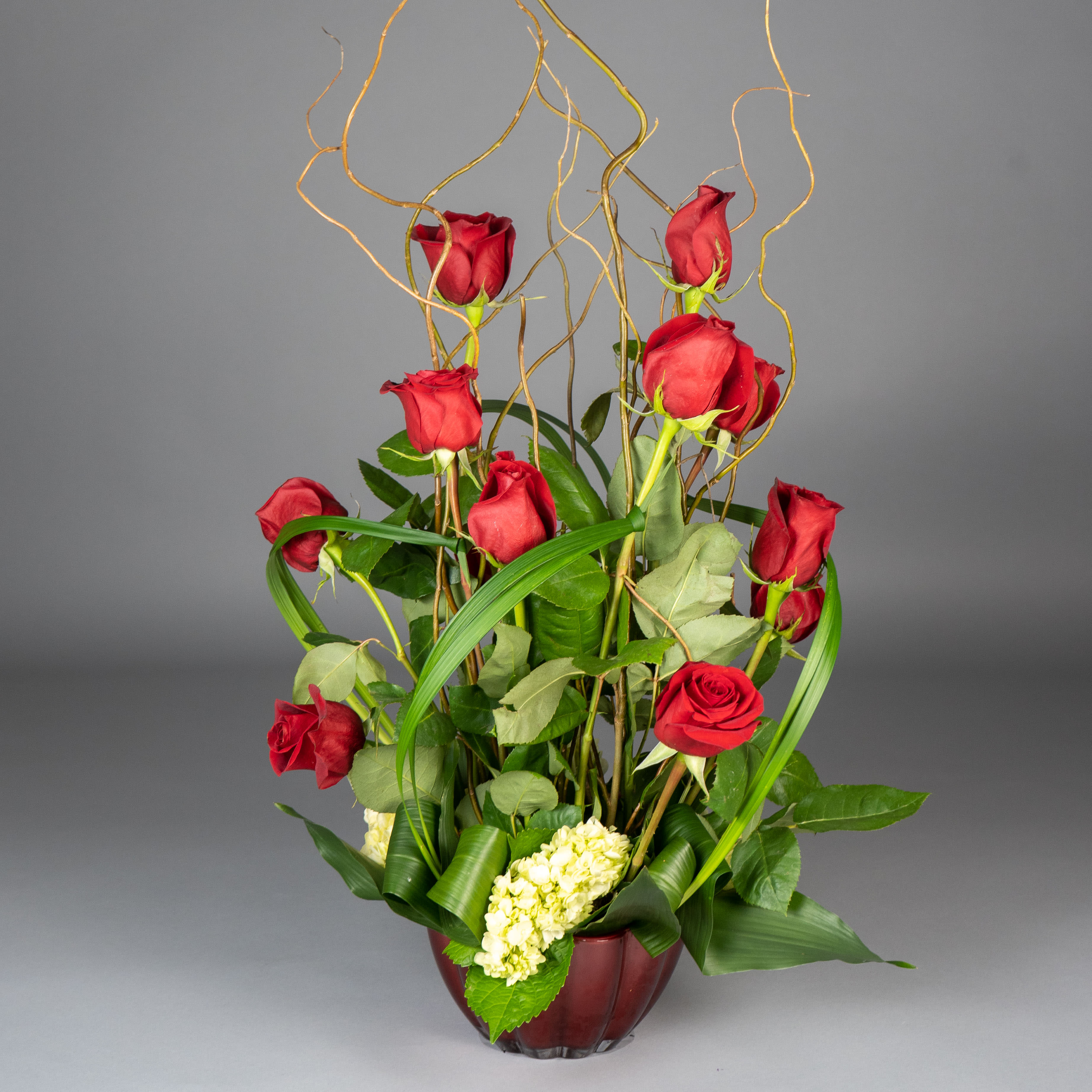 Crazy Modern Dozen Crazy Modern Dozen - Make a bold statement with this stunning arrangement of one dozen long-stemmed red roses, expertly arranged in a contemporary vase with curly willow and tropical foliage. The perfect way to show your love and impress your significant other.