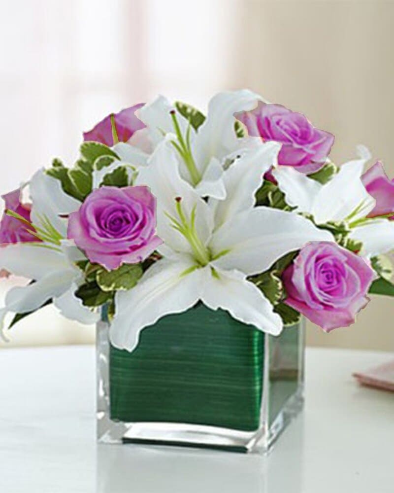 [TT-MOMEMB]:  MOTHERS EMBRACE - WHITE ORIENTAL LILIES AND LAVENDER ROSES ARRANGED COMPACT IN A CLEAR GLASS CUBE LEAF LINED VASE  