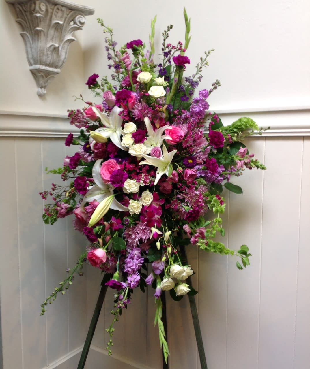 Harmonious Harmonious - This easel spray is full of roses, lilies, orchids and carnations. With lavender, white, green and pink flowers. This soft feminine piece is a beautiful addition to any memorial or celebration of life.