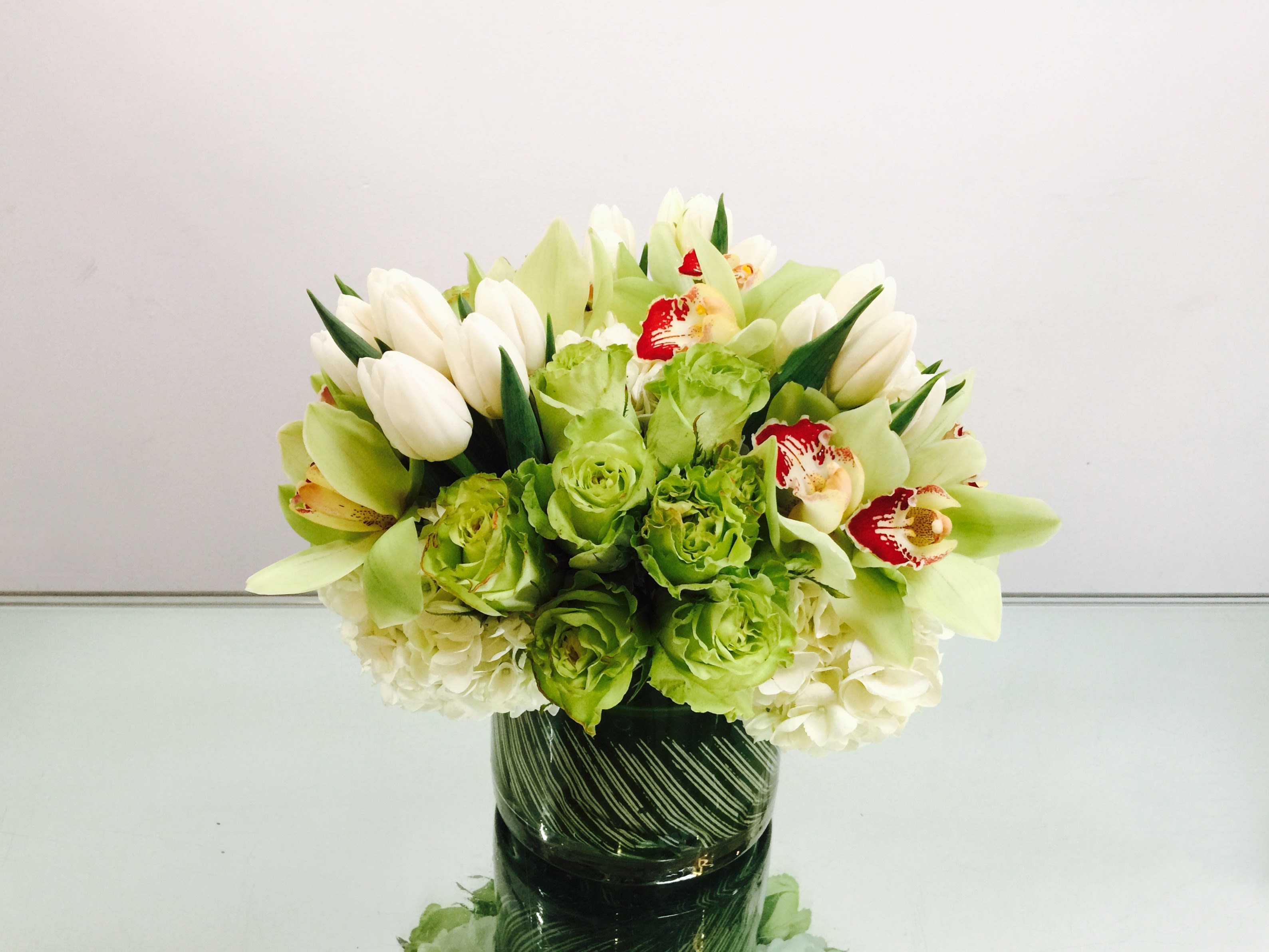 Spring Sweet - Fresh green arrangement with white tulips, pale green roses, green cymbidium, and white hydrangeas in a decorative glass vase.