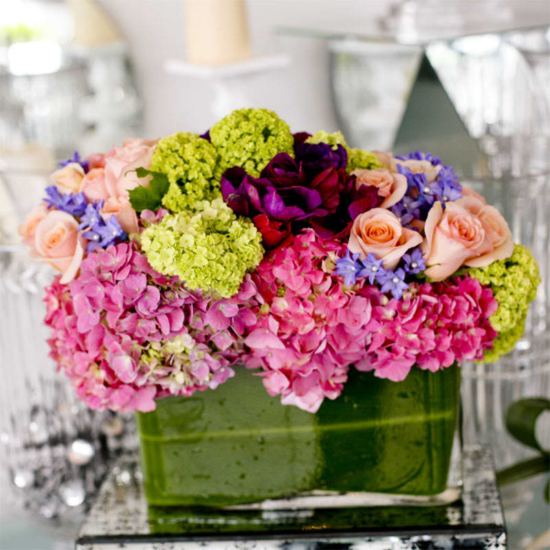Faberge - A bright combination of various colors of hydrangea with roses and a spray of other seasonal springtime flowers in a longer leaf lined vase.