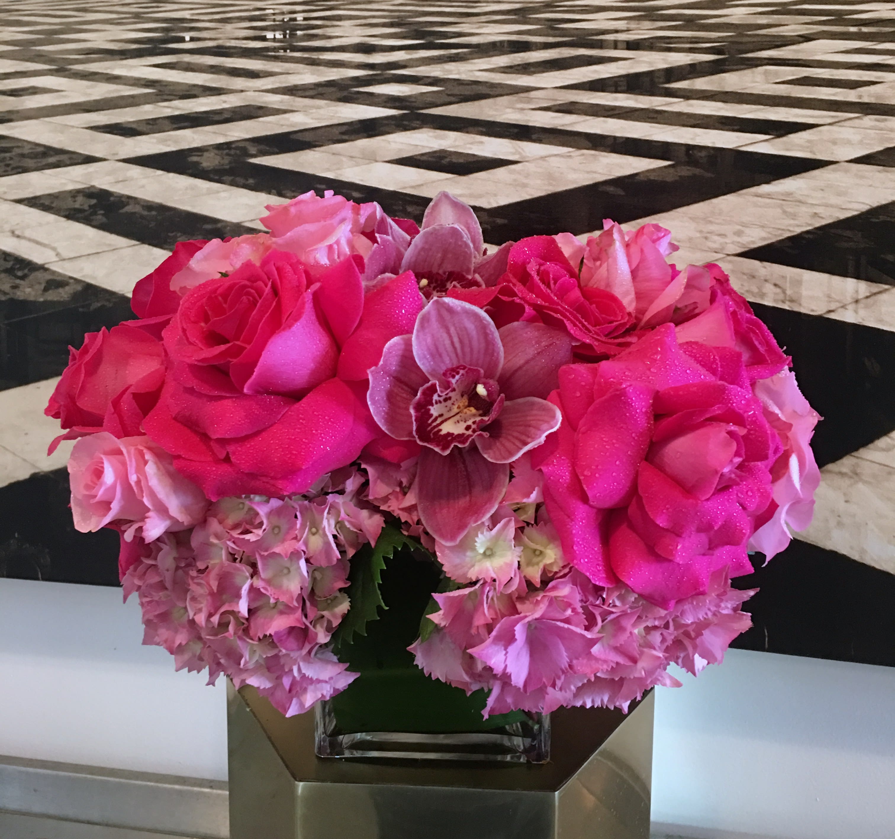 Hot Pink - PINK! Brilliant pink roses, pastel pink roses, soft pink hydrangea, and deep pink cymbidium orchids come together to create a masterpiece that is truly a masterpiece of PINK. This bright and lush arrangement sits in a leaf-lined 5x5&quot; square vase.