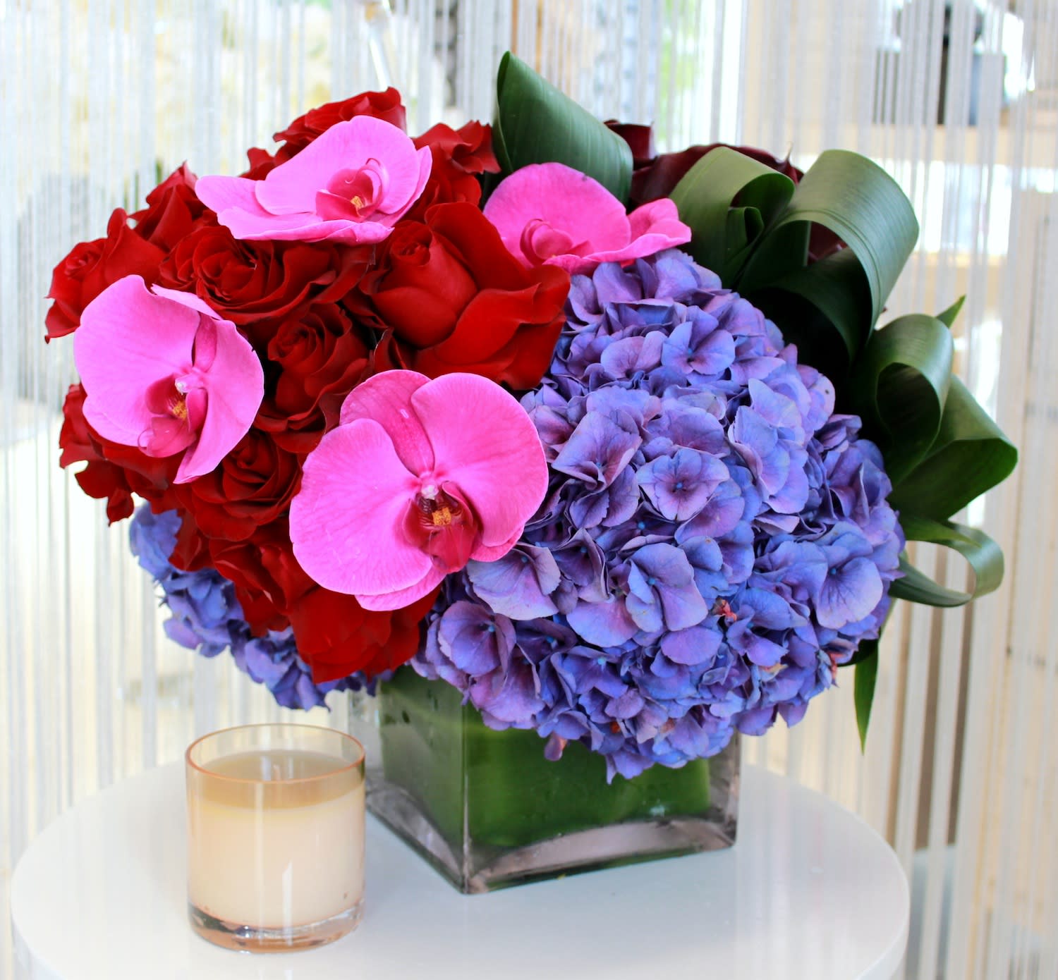 Jeweled Love - Vibrant jewel tones of magenta phalaenopsis orchids, purple hydrangeas, and deep red roses in a 5x5&quot; leaf-lined glass vase. This is an arrangement that's perfect for adding a bright splash of color anywhere ... even in the heart of that special someone!